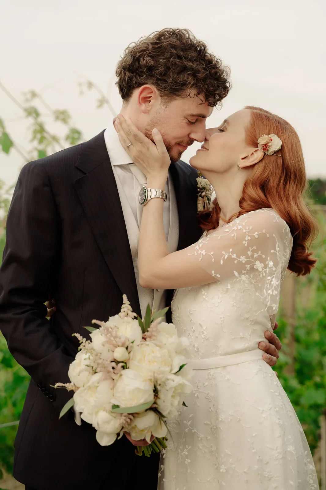 La sposa accarezza il viso dello sposo, con un bouquet di peonie bianche