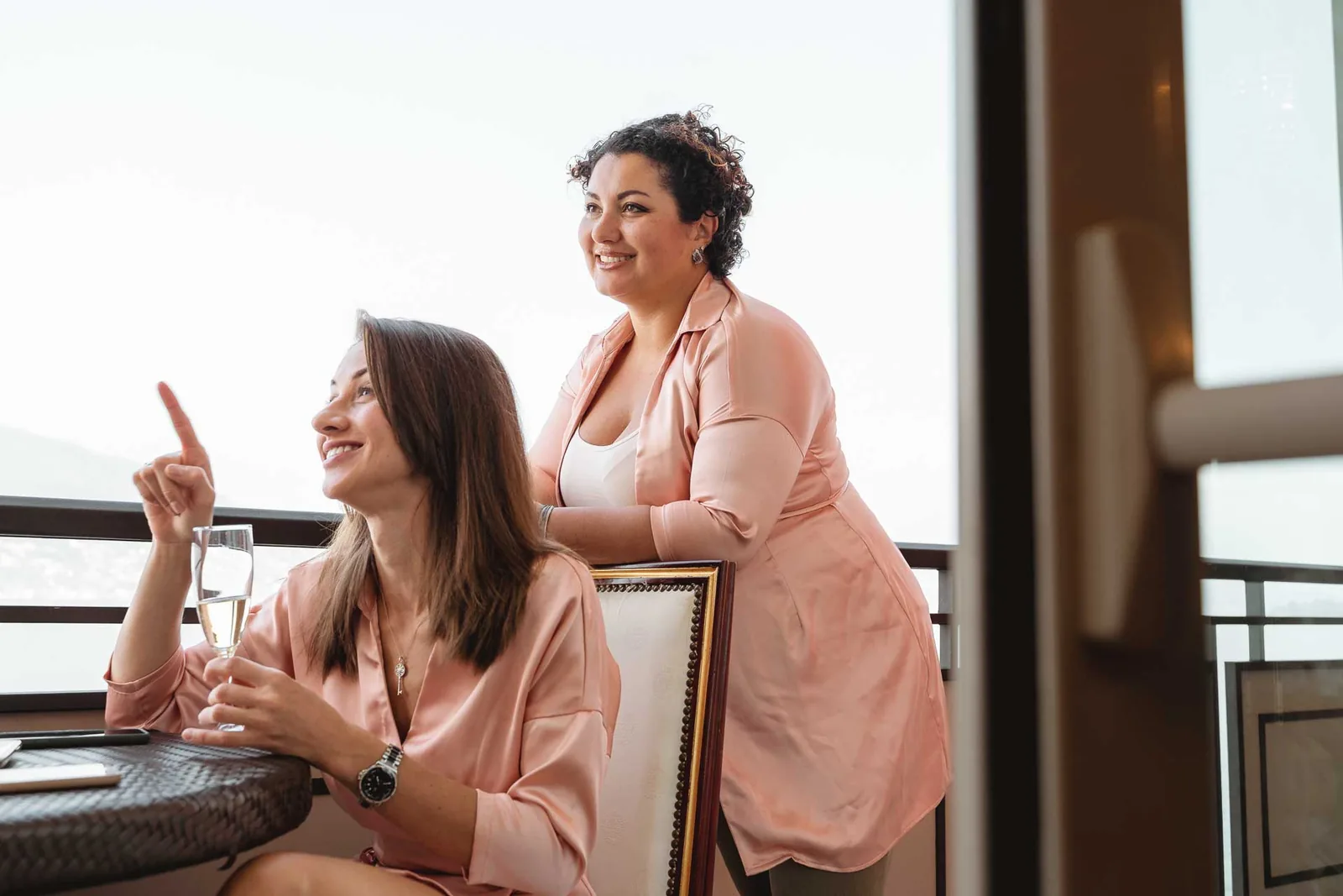 Due amiche ridono sul balcone con i calici in mano