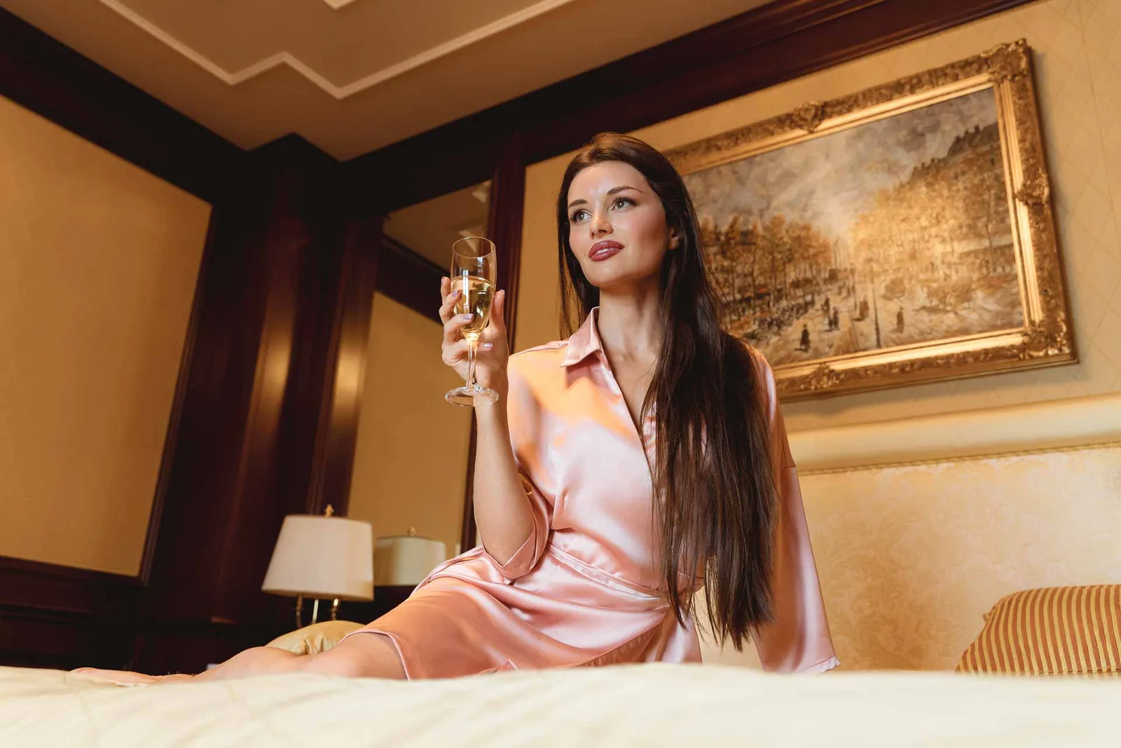 La sposa seduta sul letto con un calice, in vestaglia rosa