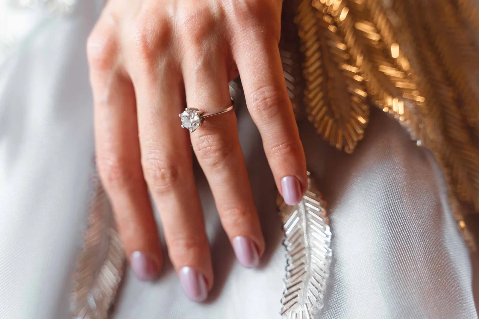 La mano della sposa con l'anello, sulle piume ricamate dell'abito