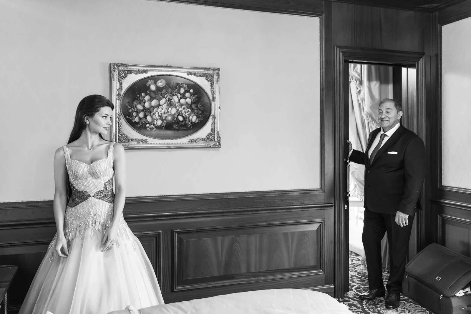 In bianco e nero, la sposa nella camera e un uomo in abito scuro che la guarda dalla porta