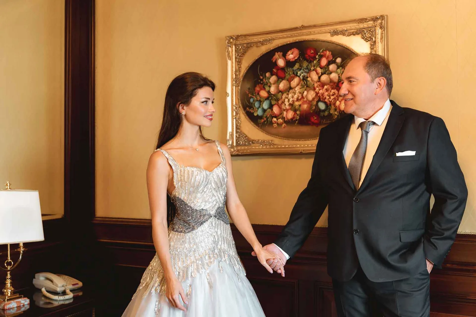 La sposa e un uomo in abito scuro mano nella mano, nella camera