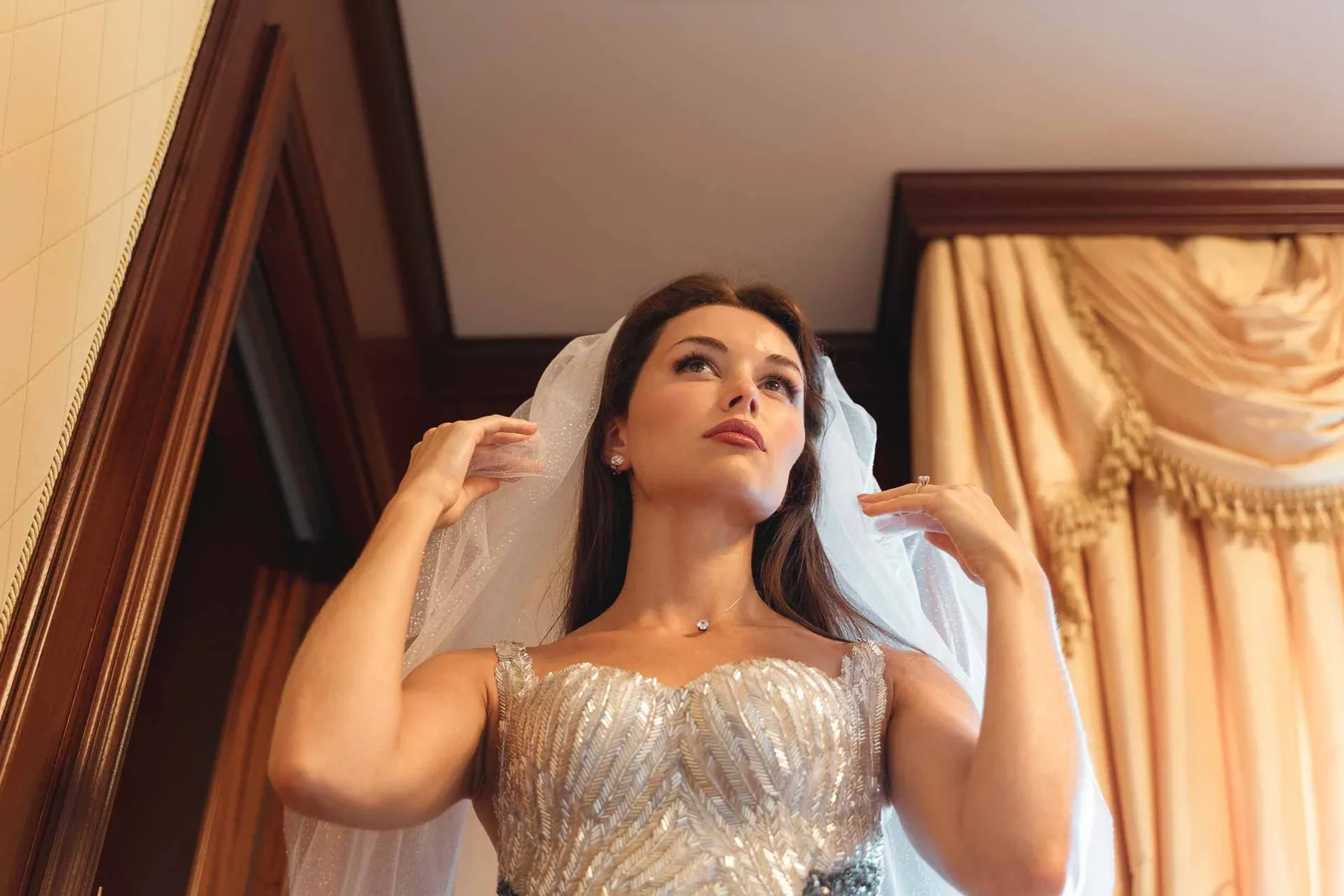 La sposa sistema il velo, tra i tendaggi della camera