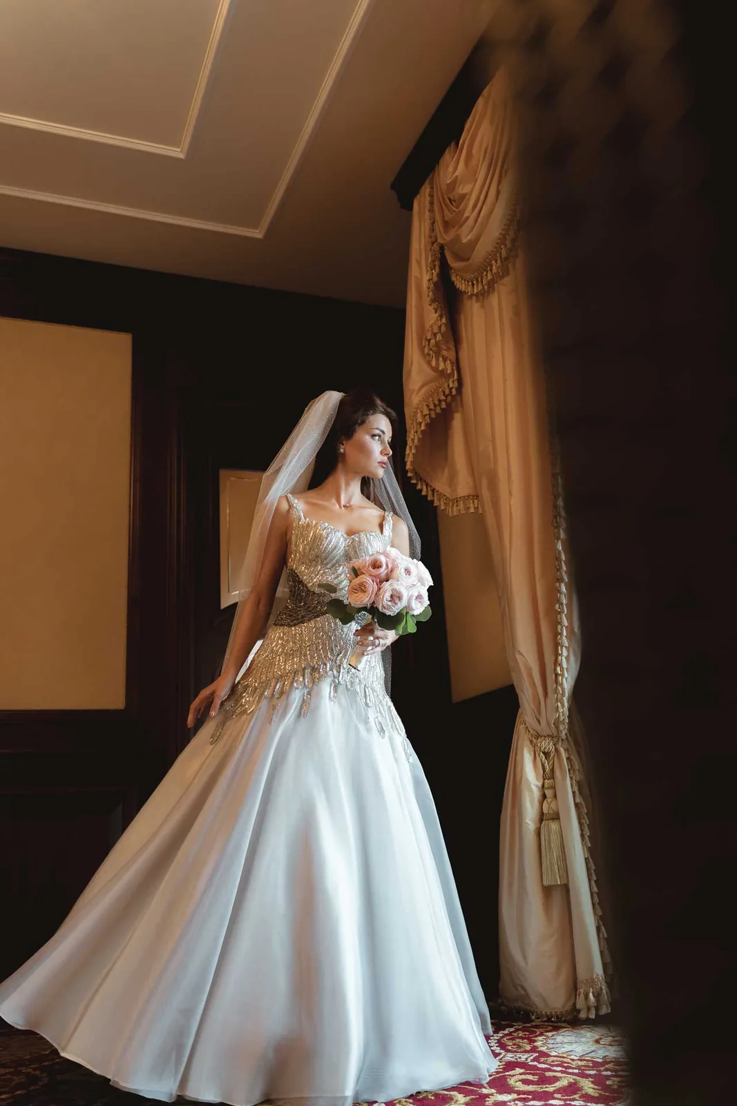 La sposa con il bouquet, in piedi davanti alla finestra della camera