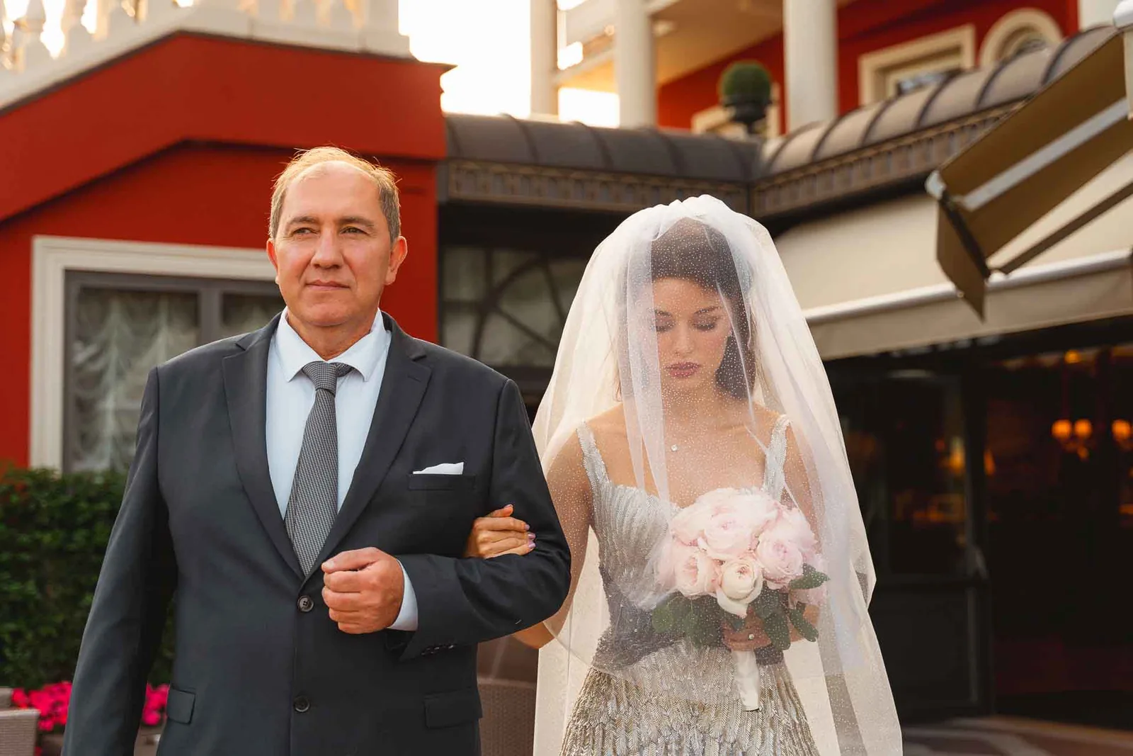 La sposa, con il velo sul viso, arriva alla cerimonia sottobraccio