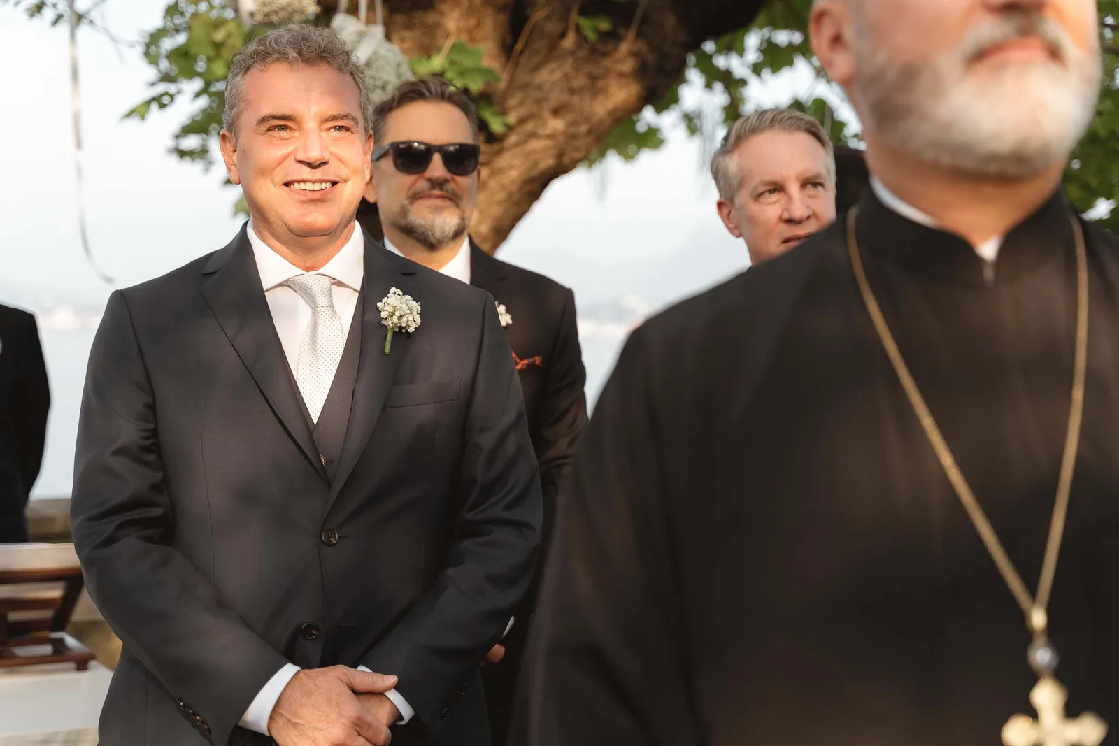 Lo sposo sorride in attesa, accanto al celebrante e agli amici
