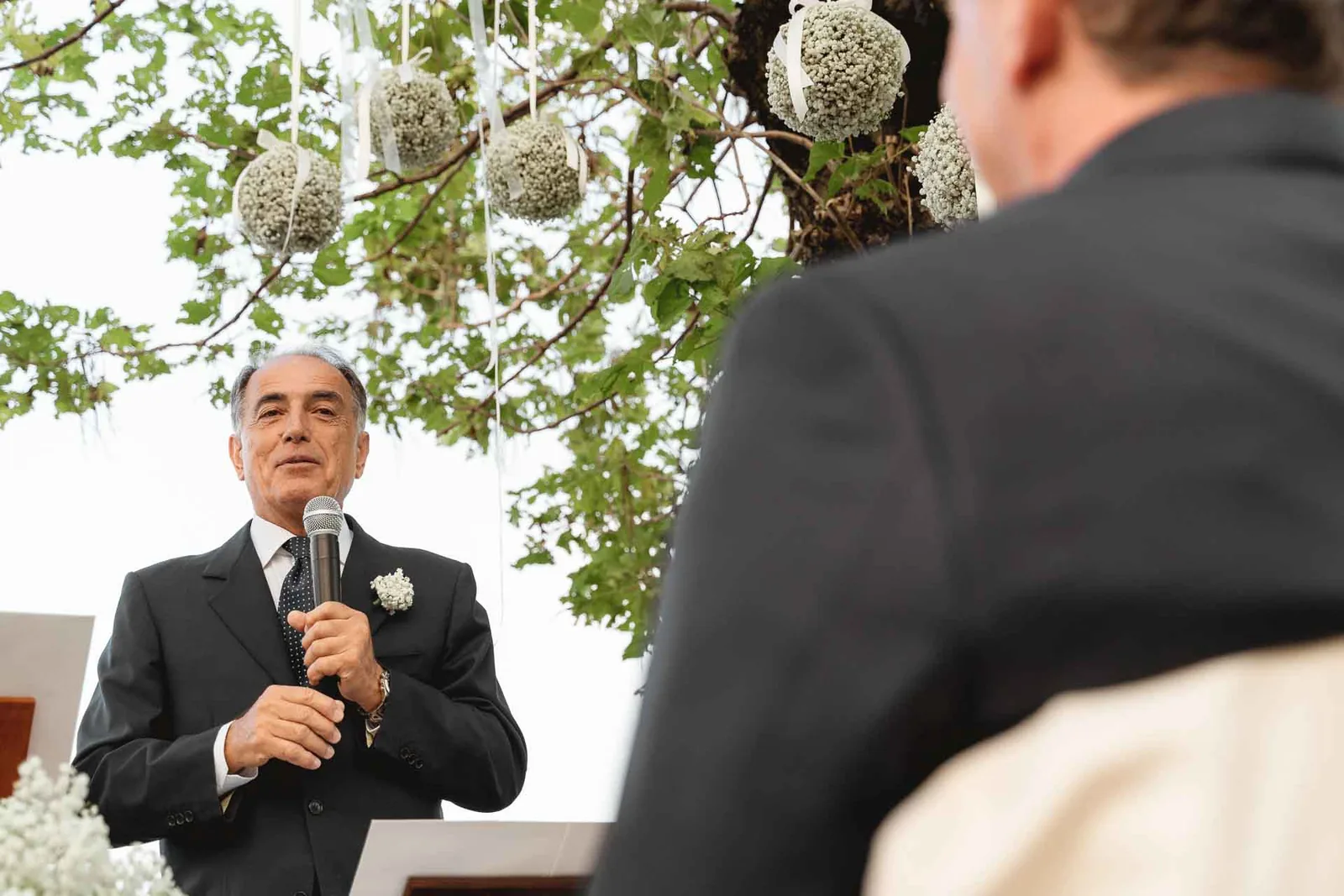 Un invitato fa un discorso al microfono sotto gli alberi