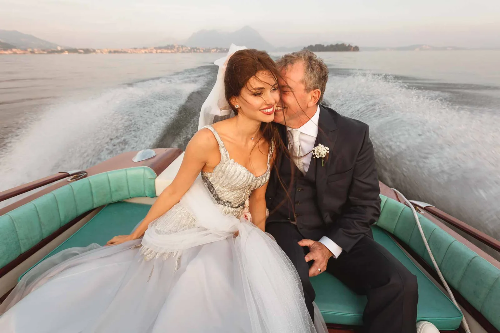 Lo sposo bacia la sposa sulla guancia, sul motoscafo che corre sul lago