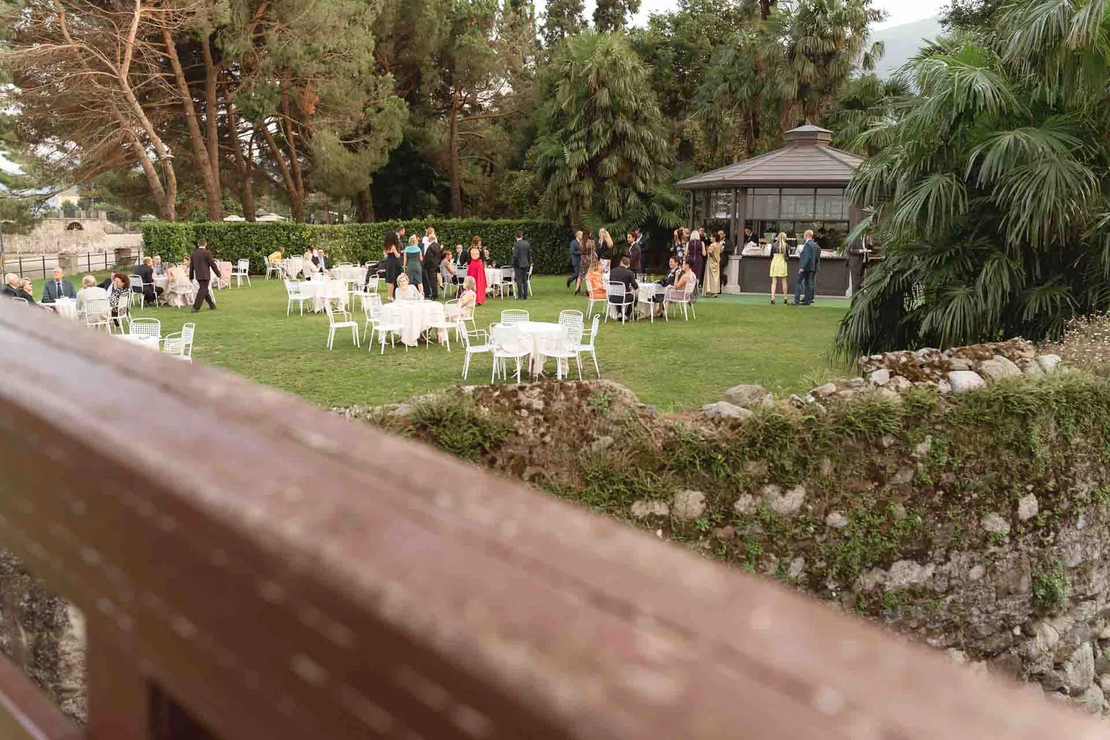 Gli invitati sul prato del giardino, oltre la ringhiera in legno