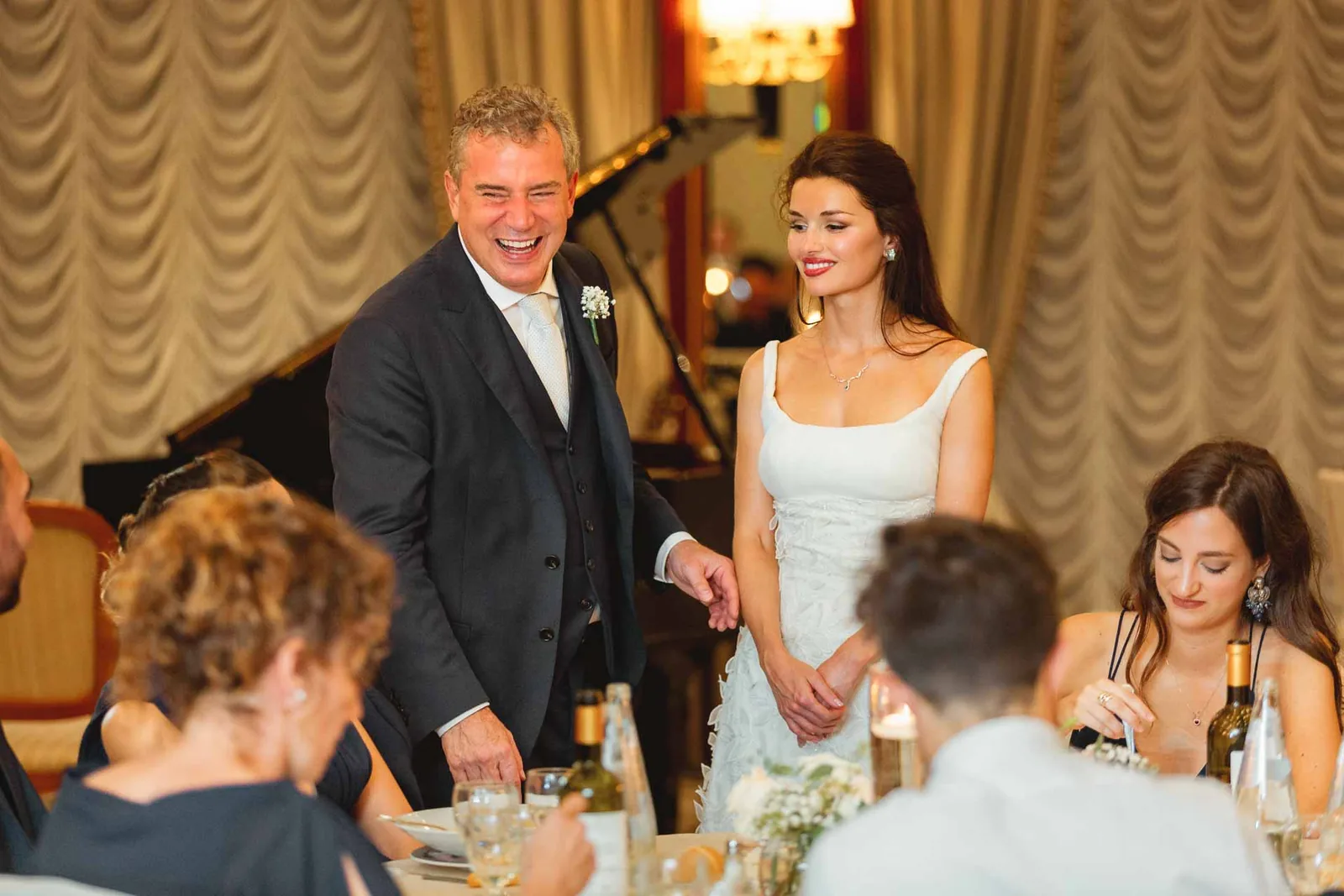 Lo sposo ride accanto alla sposa, davanti a un tavolo di invitati