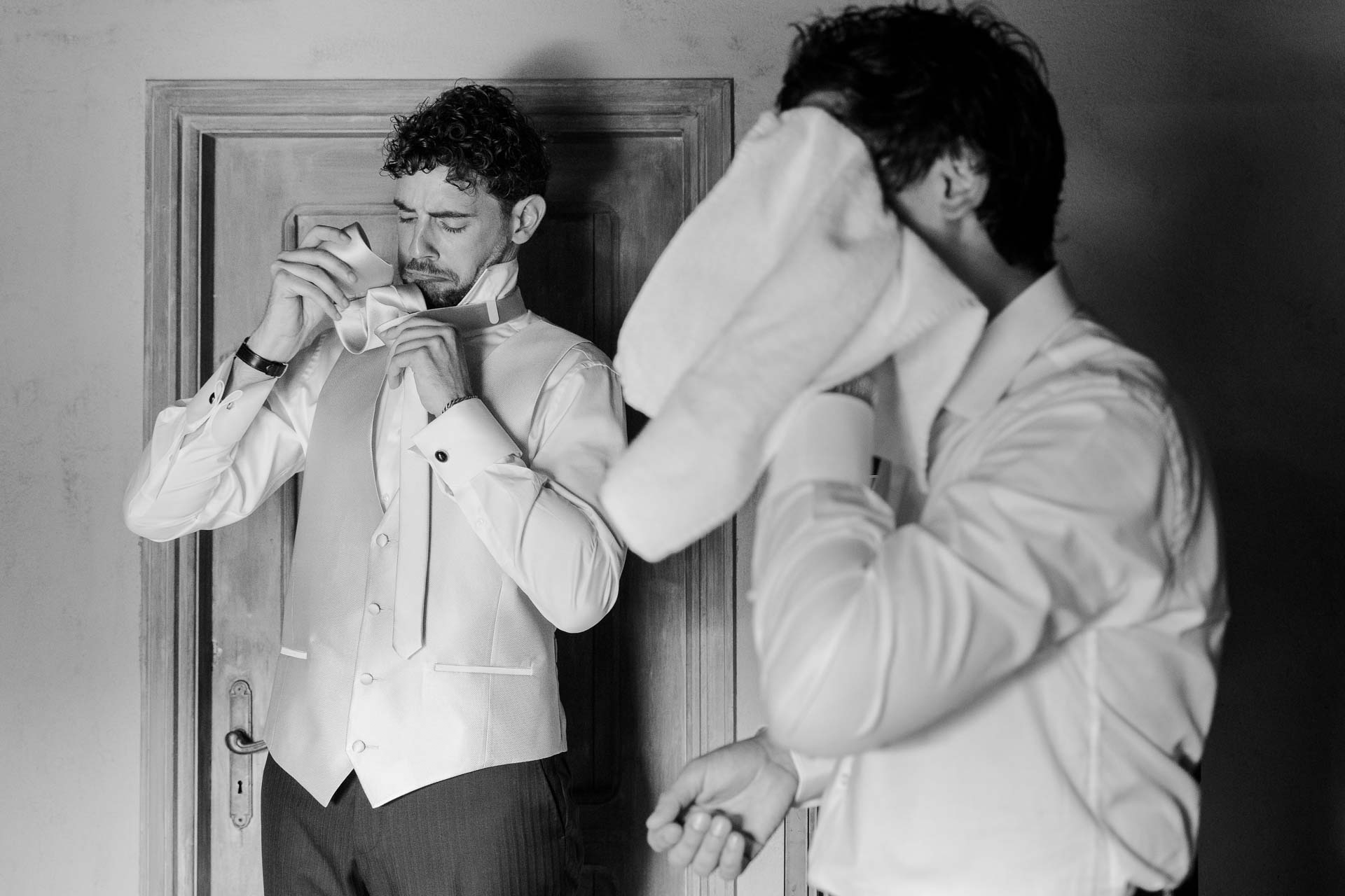 In bianco e nero, lo sposo si chiude i polsini accanto a un amico che si asciuga il viso