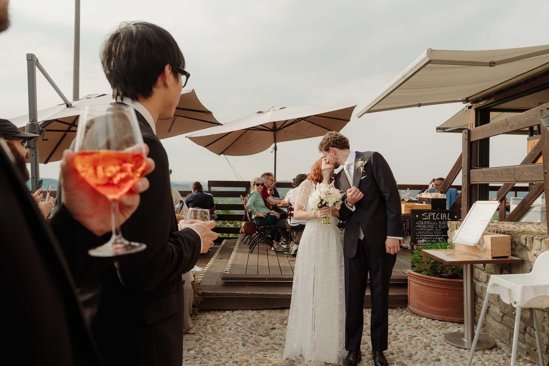 Gli sposi si baciano sulla terrazza dell'aperitivo, tra gli ombrelloni, oltre un calice di spritz