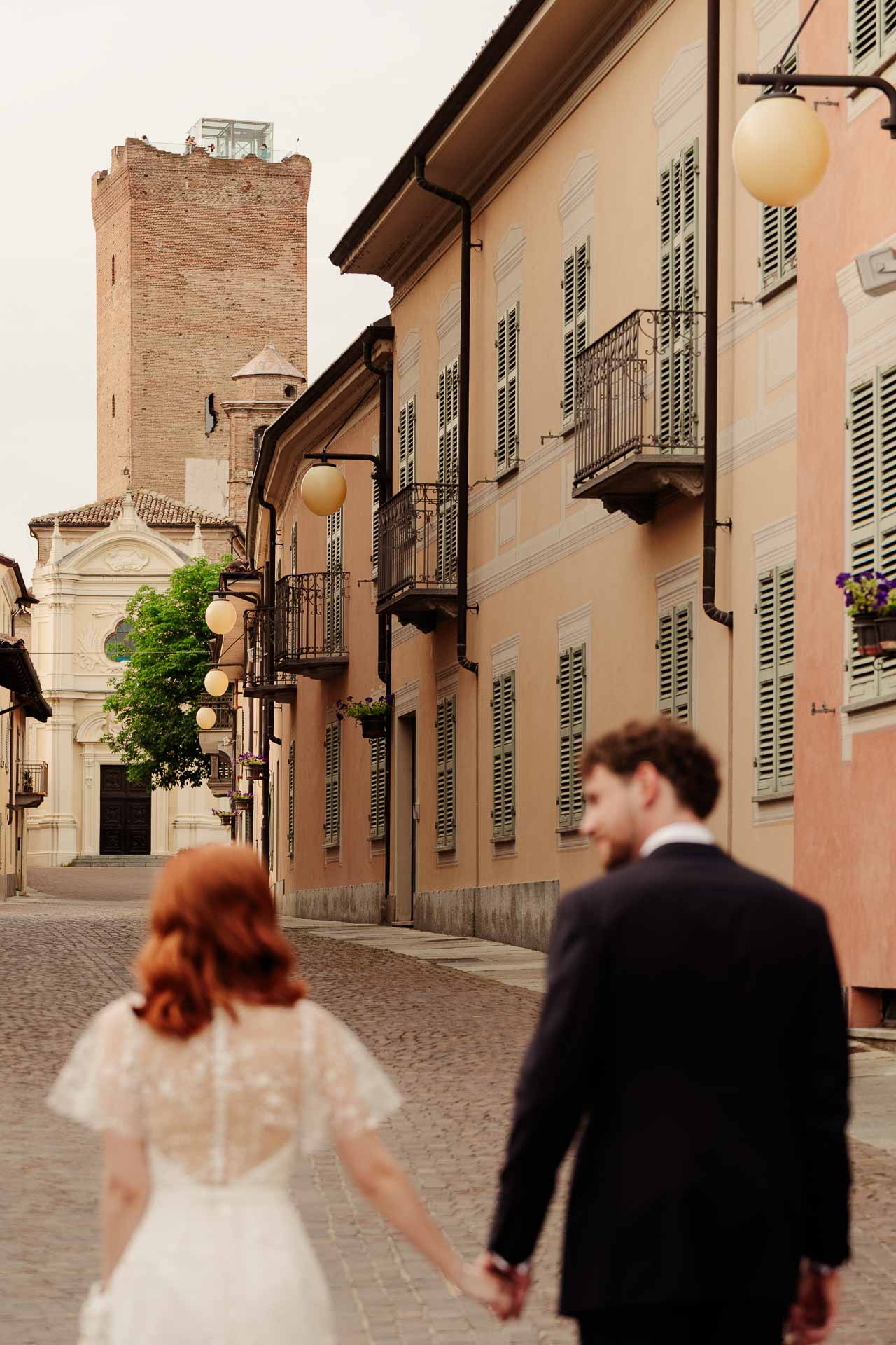 Gli sposi mano nella mano nella via di Barbaresco, verso la torre