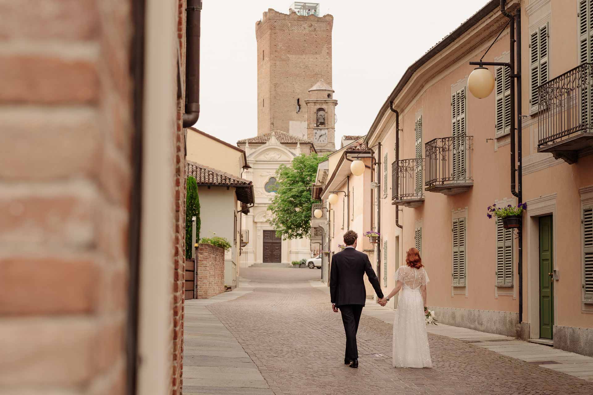 Gli sposi si allontanano mano nella mano lungo la via, verso la torre