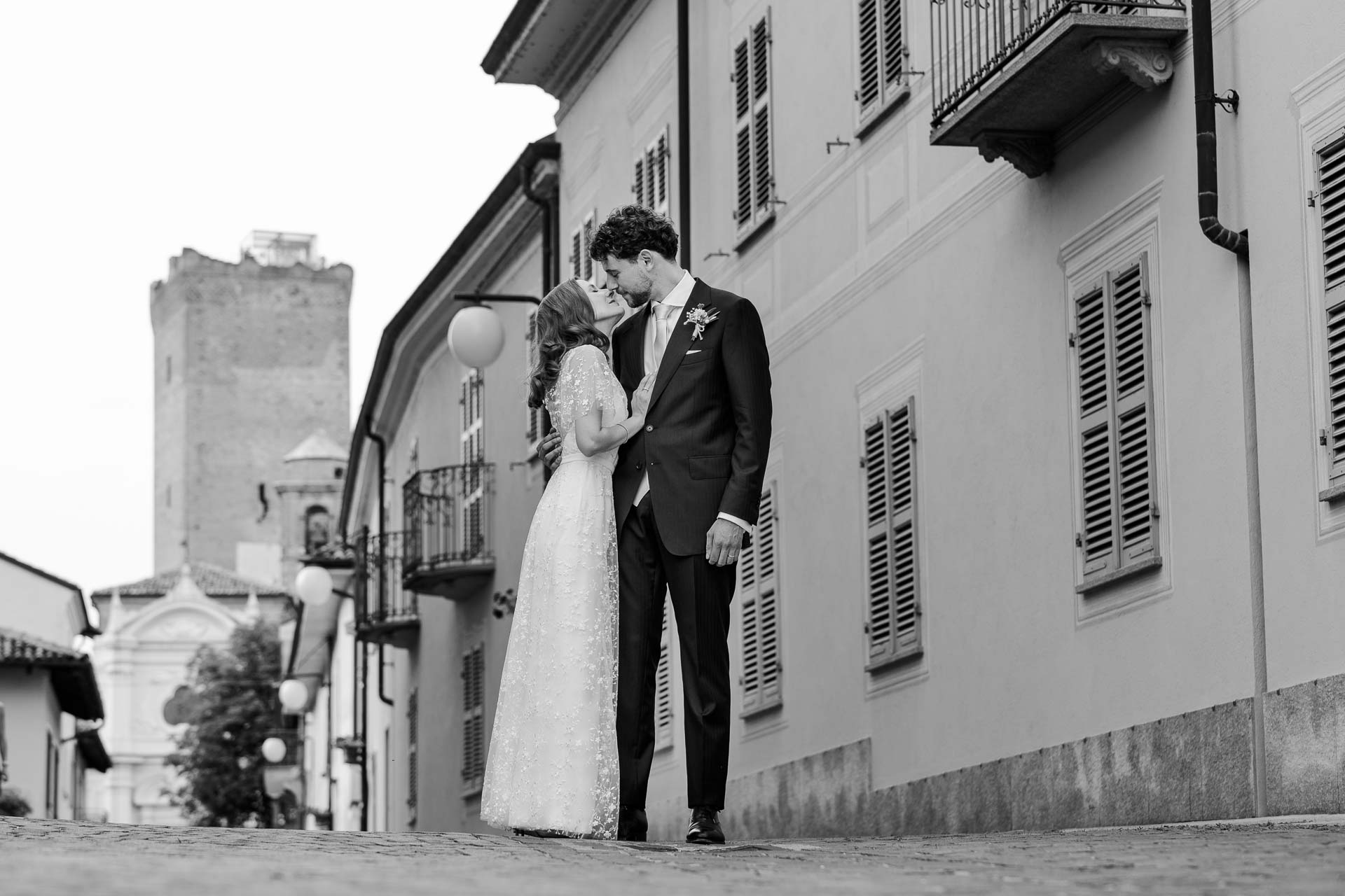 In bianco e nero, gli sposi abbracciati nella via, con la torre sullo sfondo