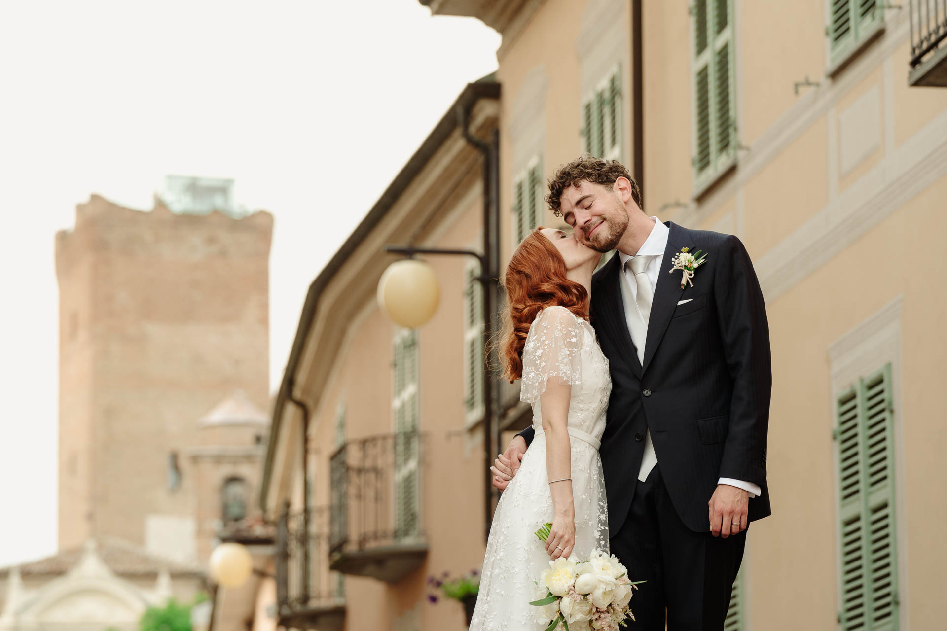 La sposa appoggia la testa sulla spalla dello sposo, tra le case di Barbaresco, con la torre in fondo