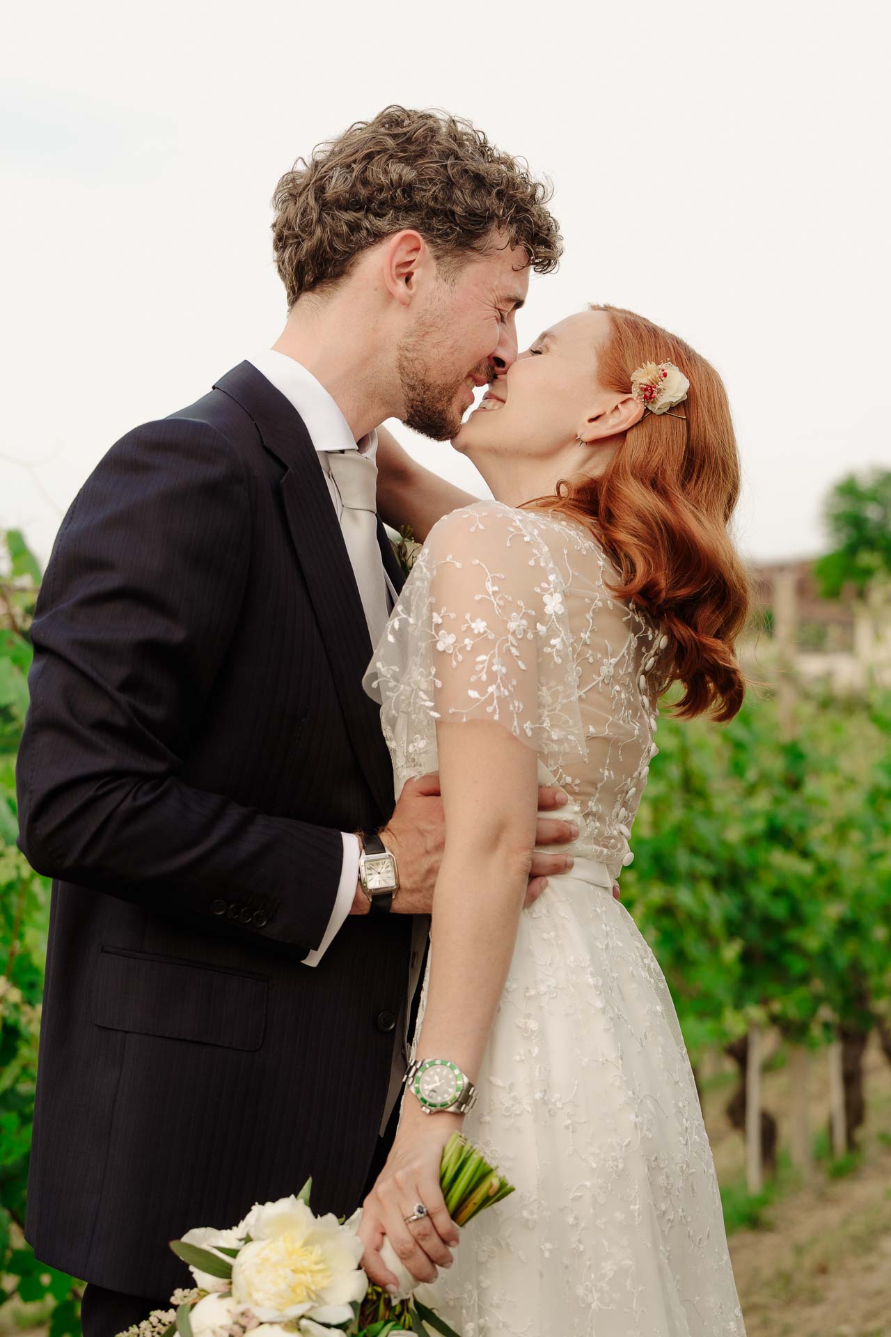Gli sposi si baciano tra le vigne, lei con il bouquet in mano