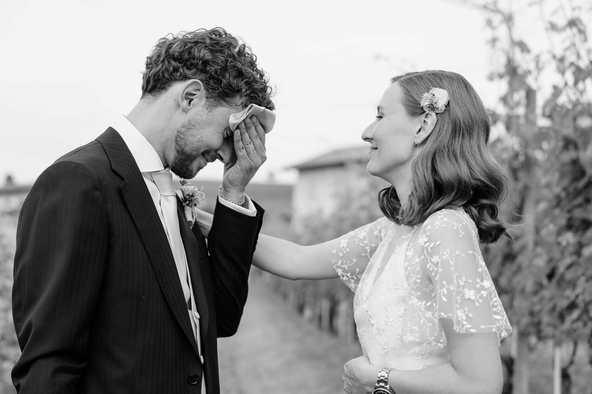 In bianco e nero, lo sposo si copre il viso, commosso, mentre la sposa ride e gli tocca il braccio