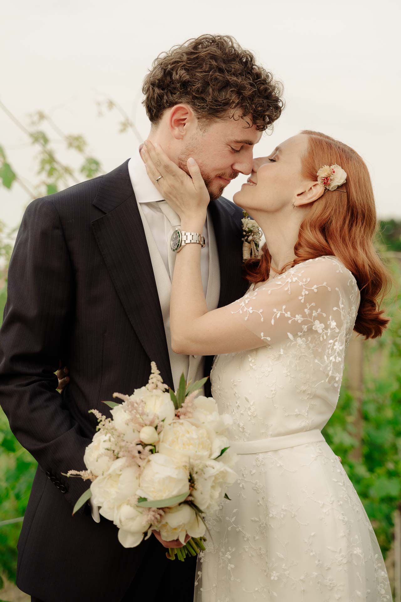 La sposa accarezza il viso dello sposo mentre si baciano, tra le vigne