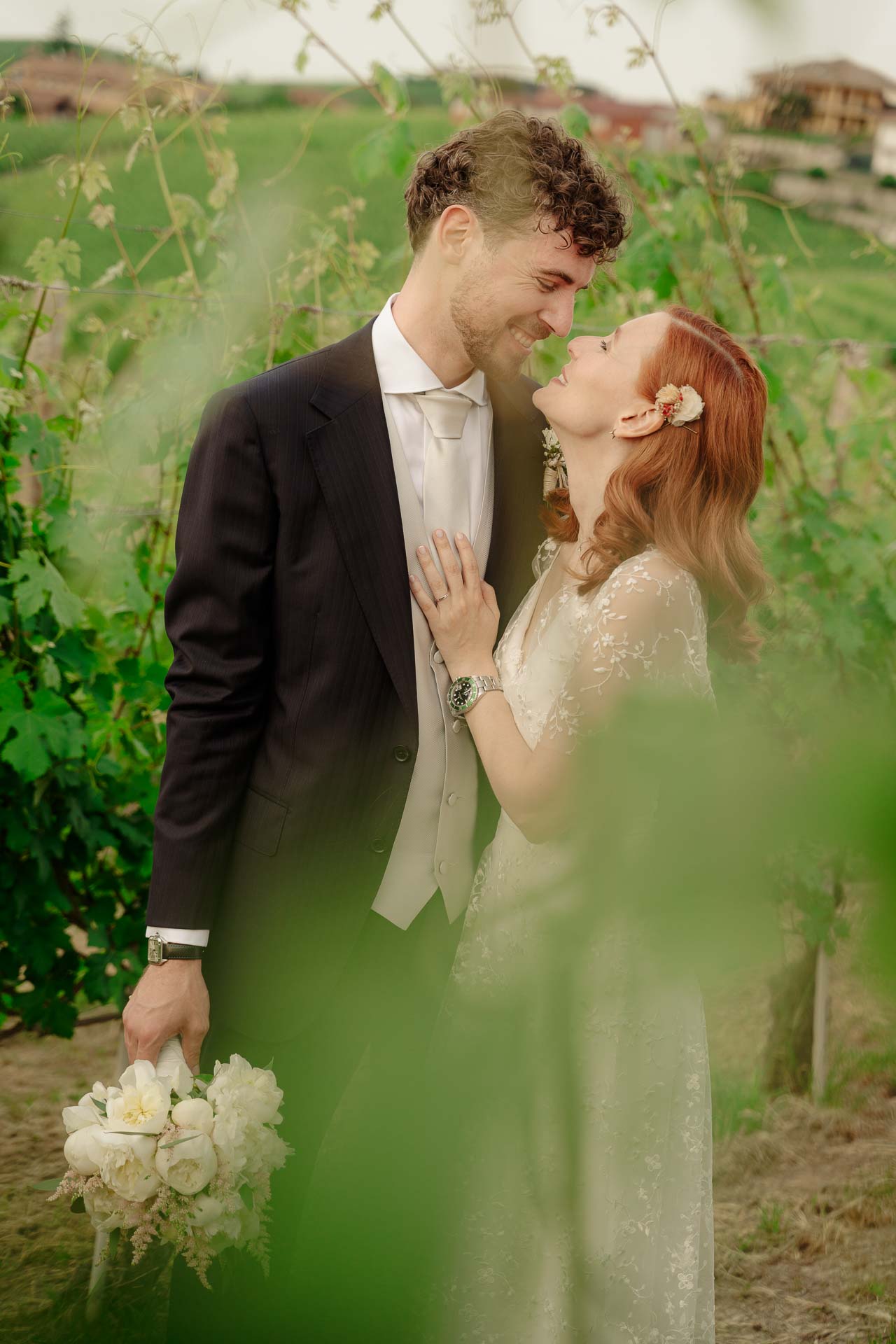 Gli sposi si sorridono tra le vigne, visti attraverso le foglie