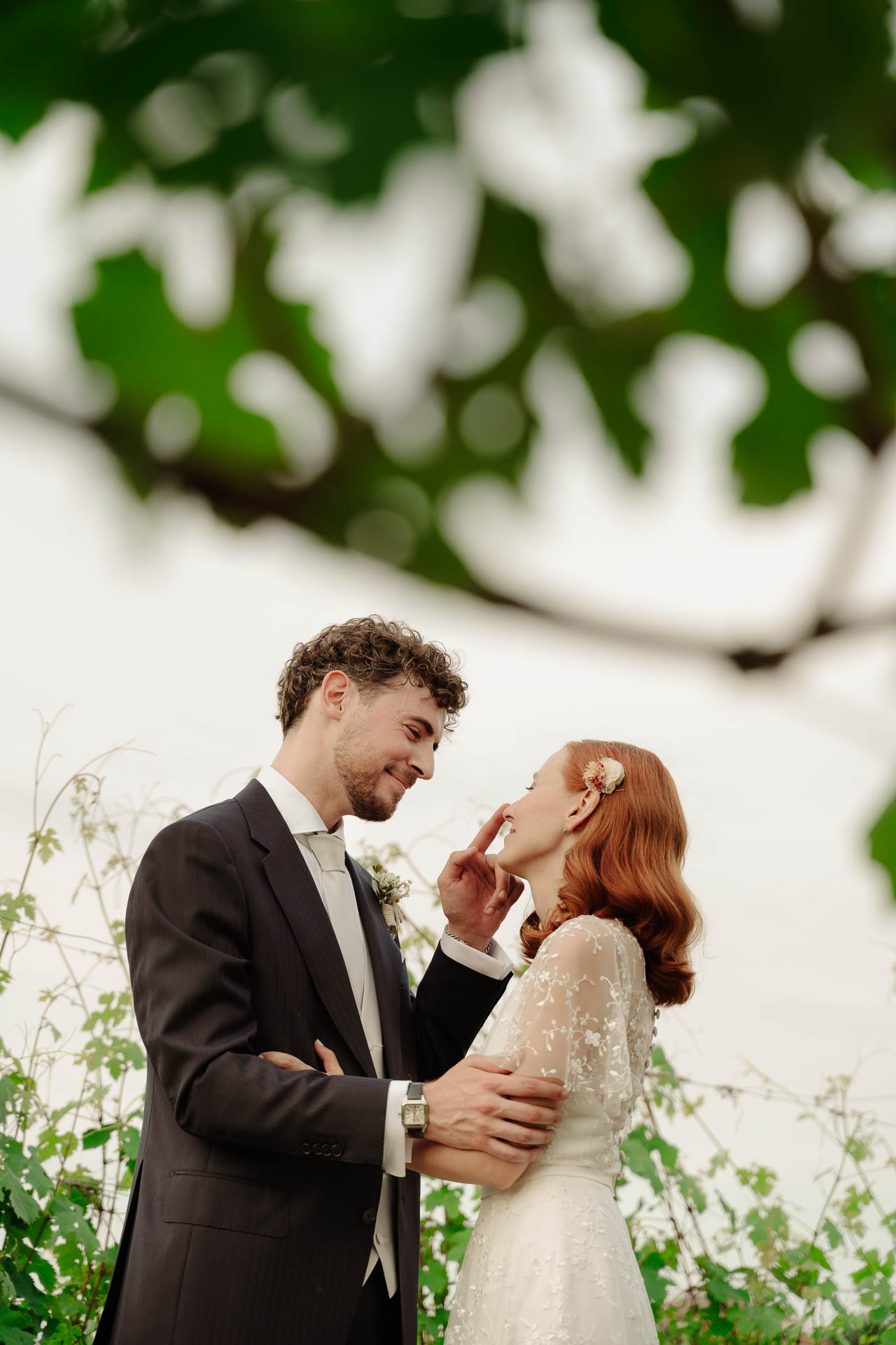 Lo sposo sfiora il viso della sposa, sotto i rami