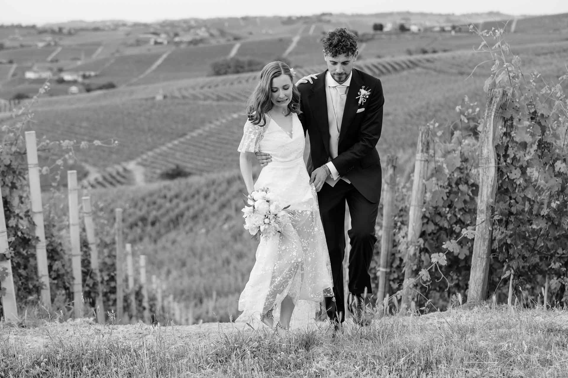 In bianco e nero, gli sposi scendono tra i filari, con le colline di vigne alle spalle