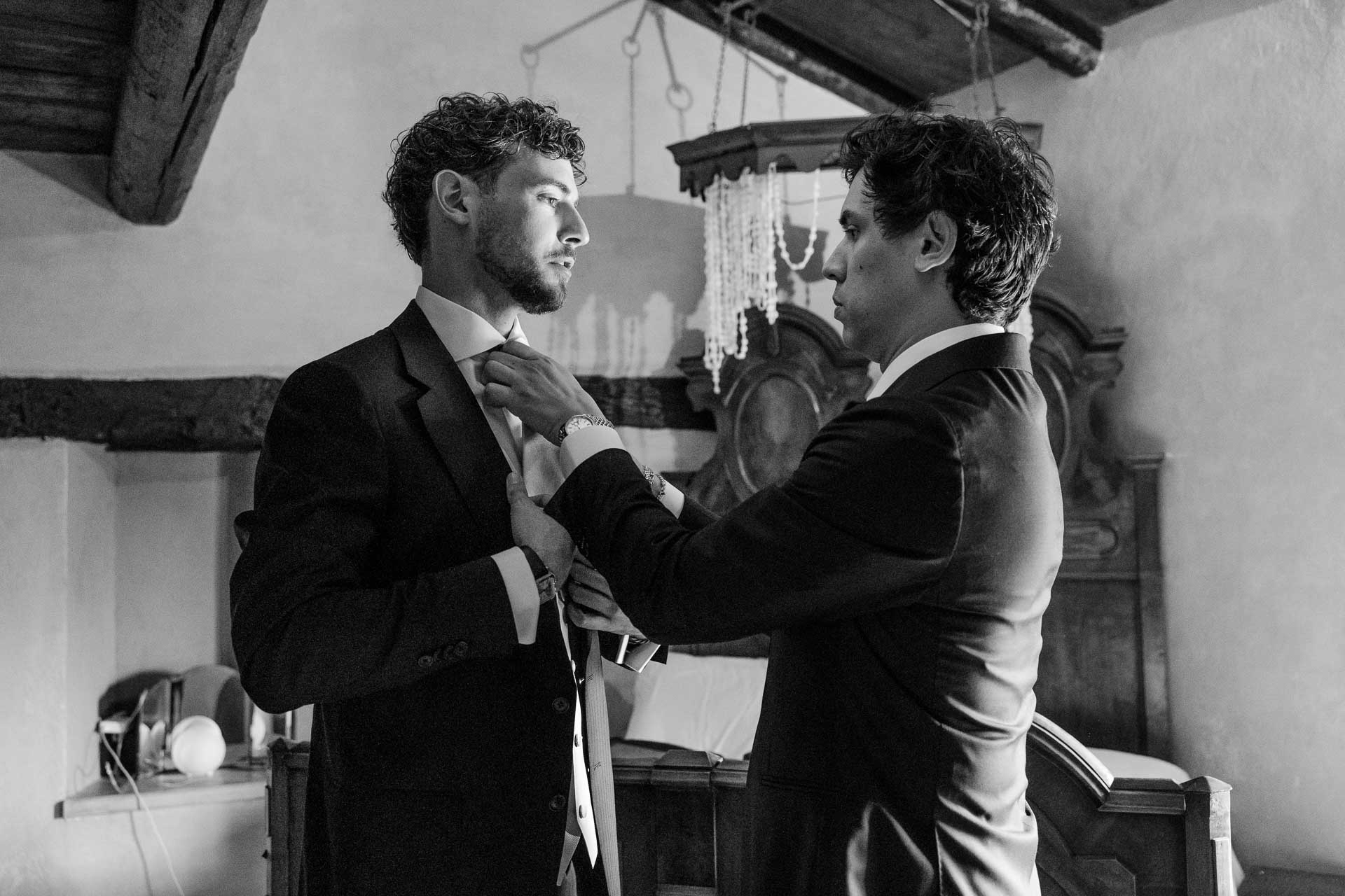 In bianco e nero, un amico sistema la cravatta allo sposo