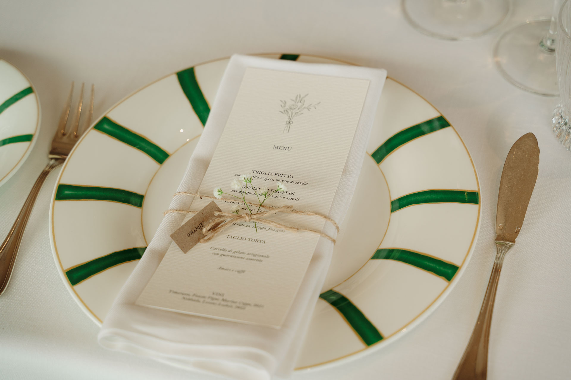 Il menu legato con lo spago sul tovagliolo, nel piatto a raggi verdi