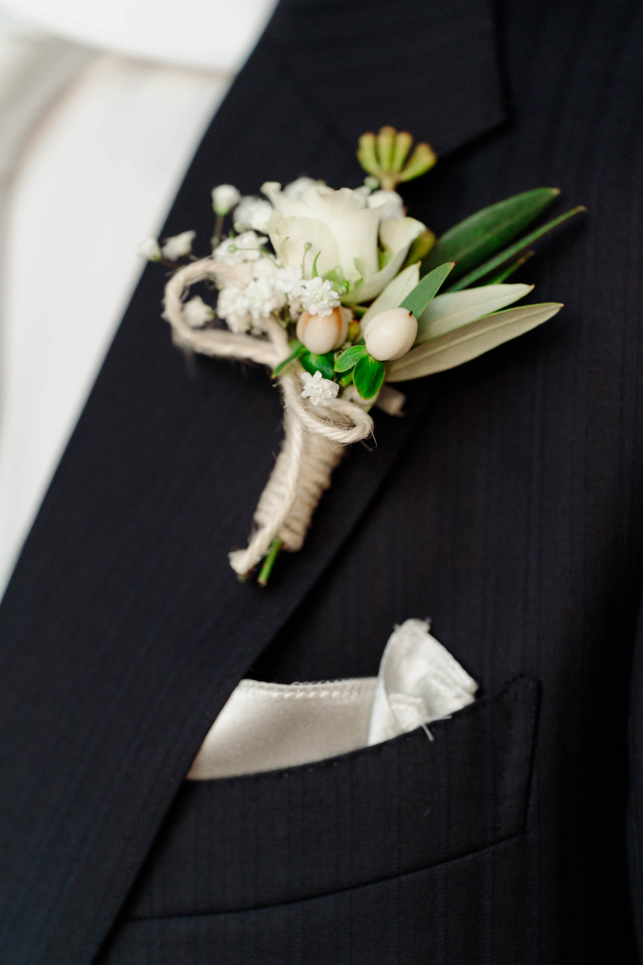 Il fiore all'occhiello di rose bianche e ulivo sulla giacca blu, con il fazzoletto nel taschino