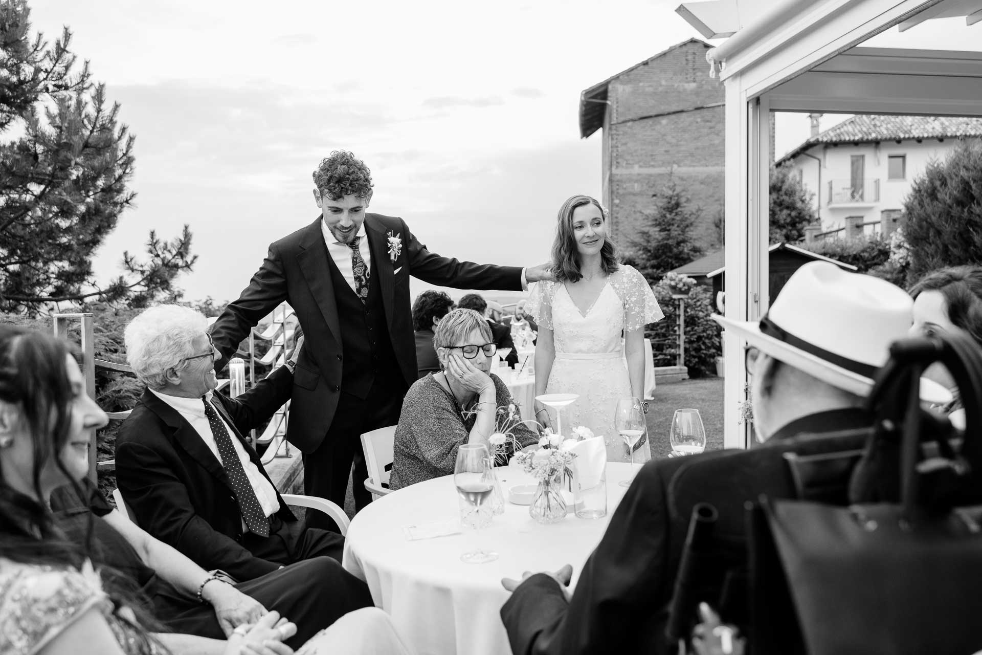 In bianco e nero, lo sposo saluta gli invitati ai tavoli, sotto la veranda