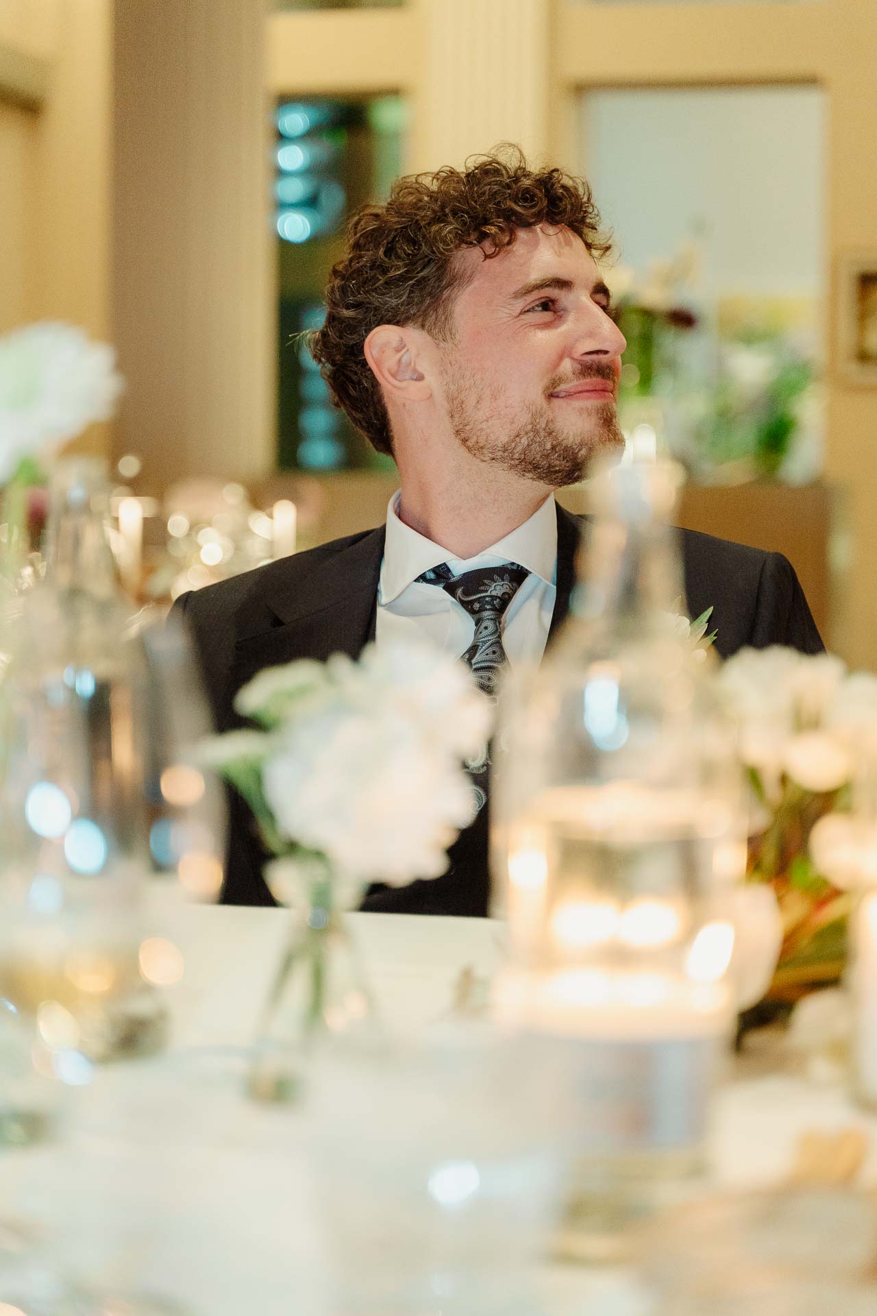 Lo sposo ascolta sorridendo, tra le candele e i fiori