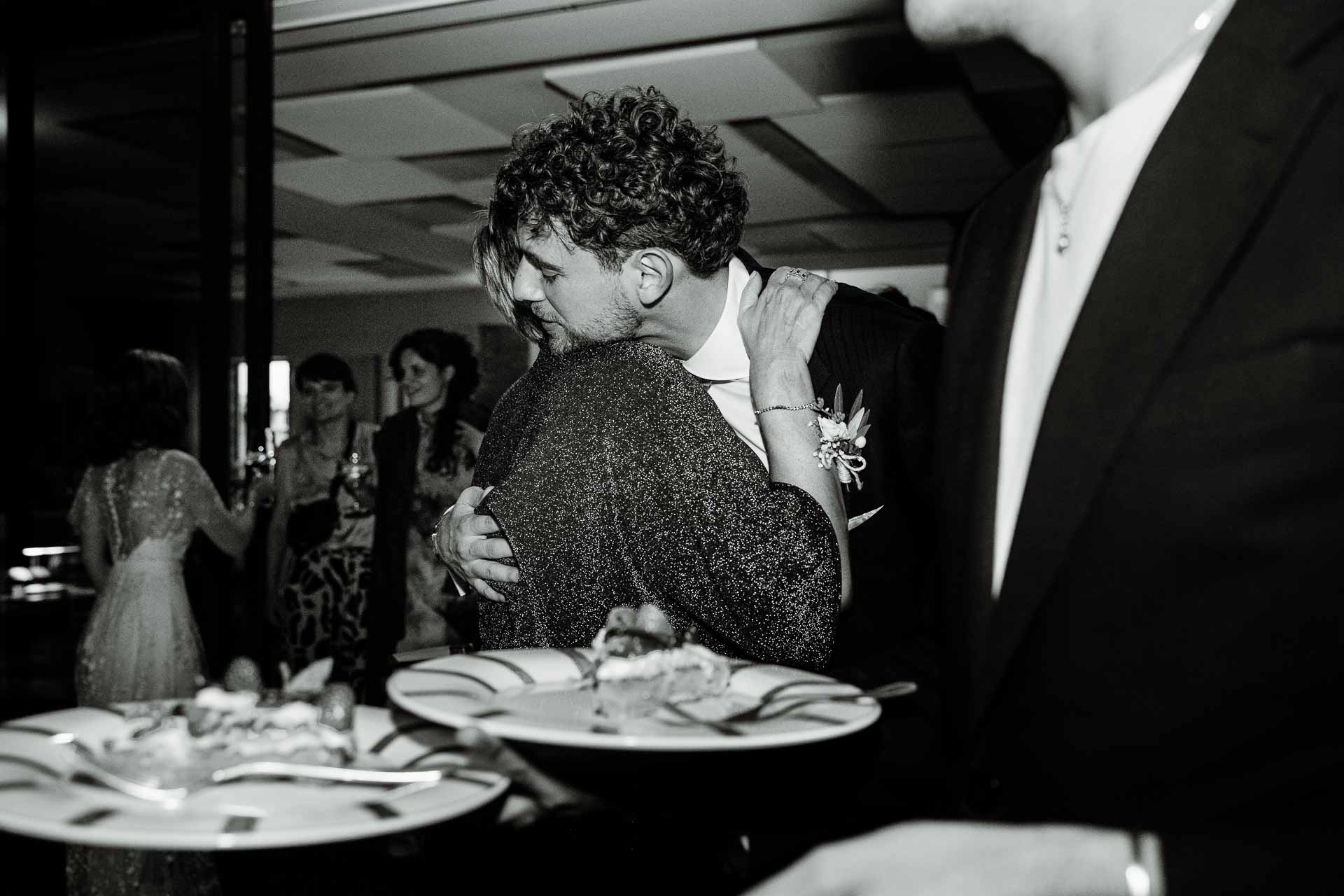 In bianco e nero, lo sposo abbraccia un'amica tra gli invitati