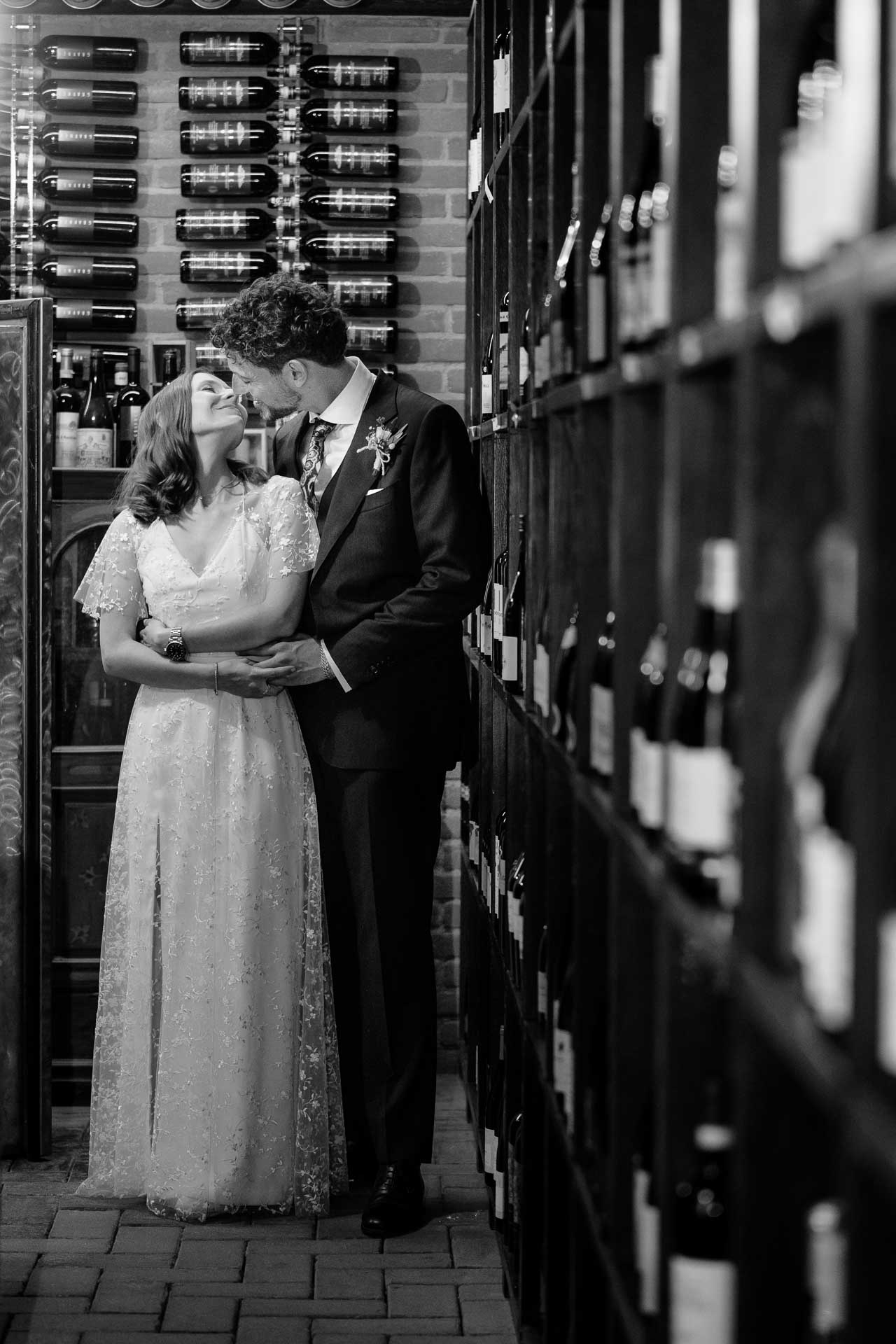 In bianco e nero, gli sposi si baciano tra gli scaffali della cantina