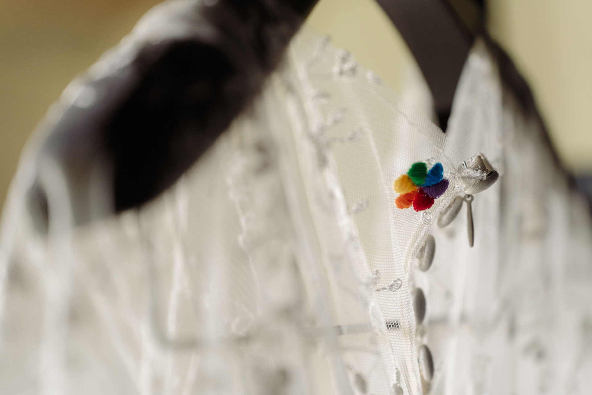 L'abito da sposa appeso, con una piccola spilla a fiore colorata