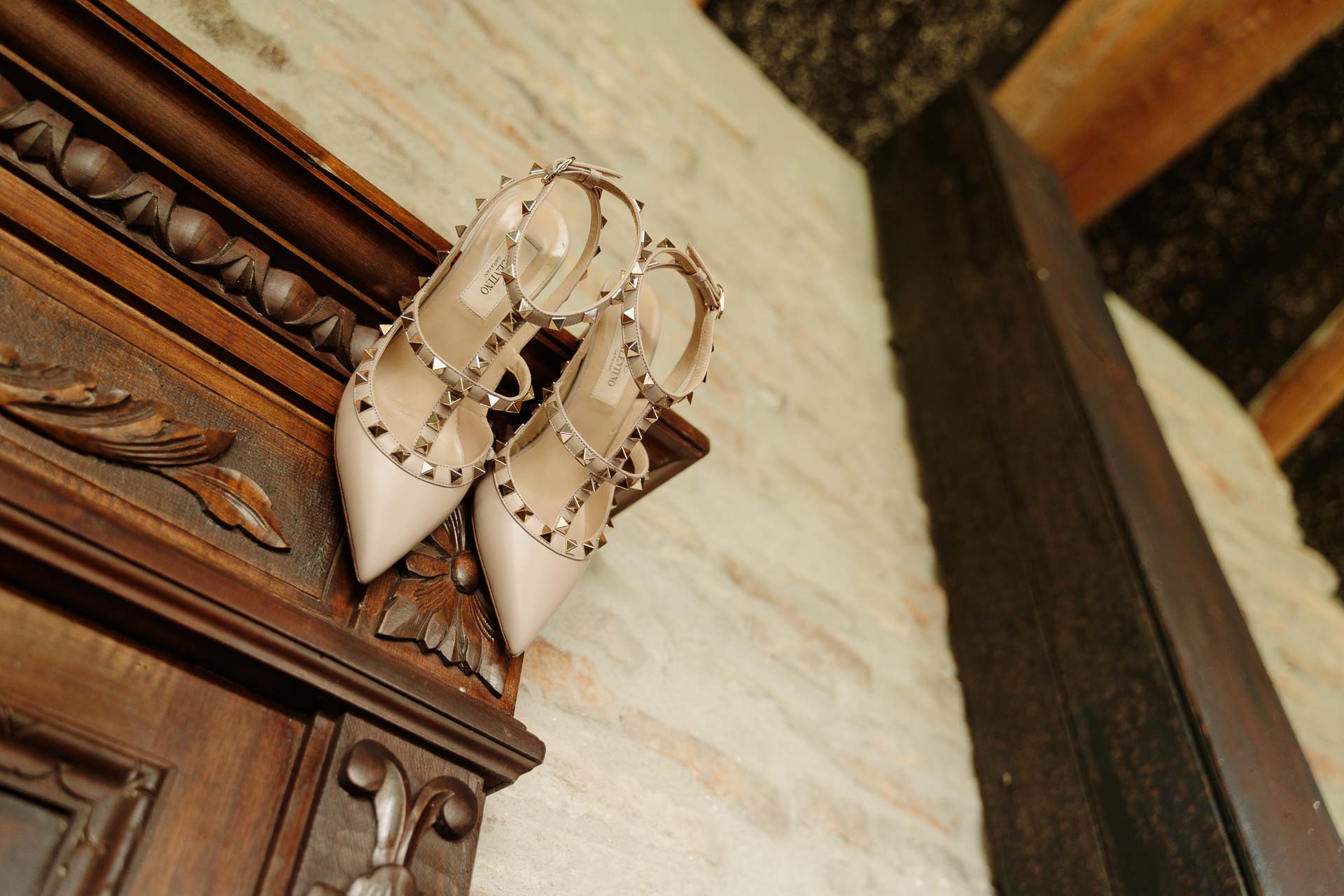 Le scarpe della sposa, color cipria con le borchie, su un mobile di legno intagliato