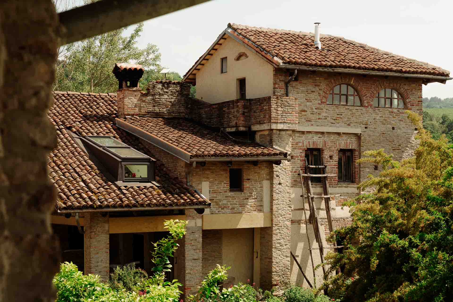 La cascina di mattoni con il tetto di coppi, tra gli alberi, vista dal portico