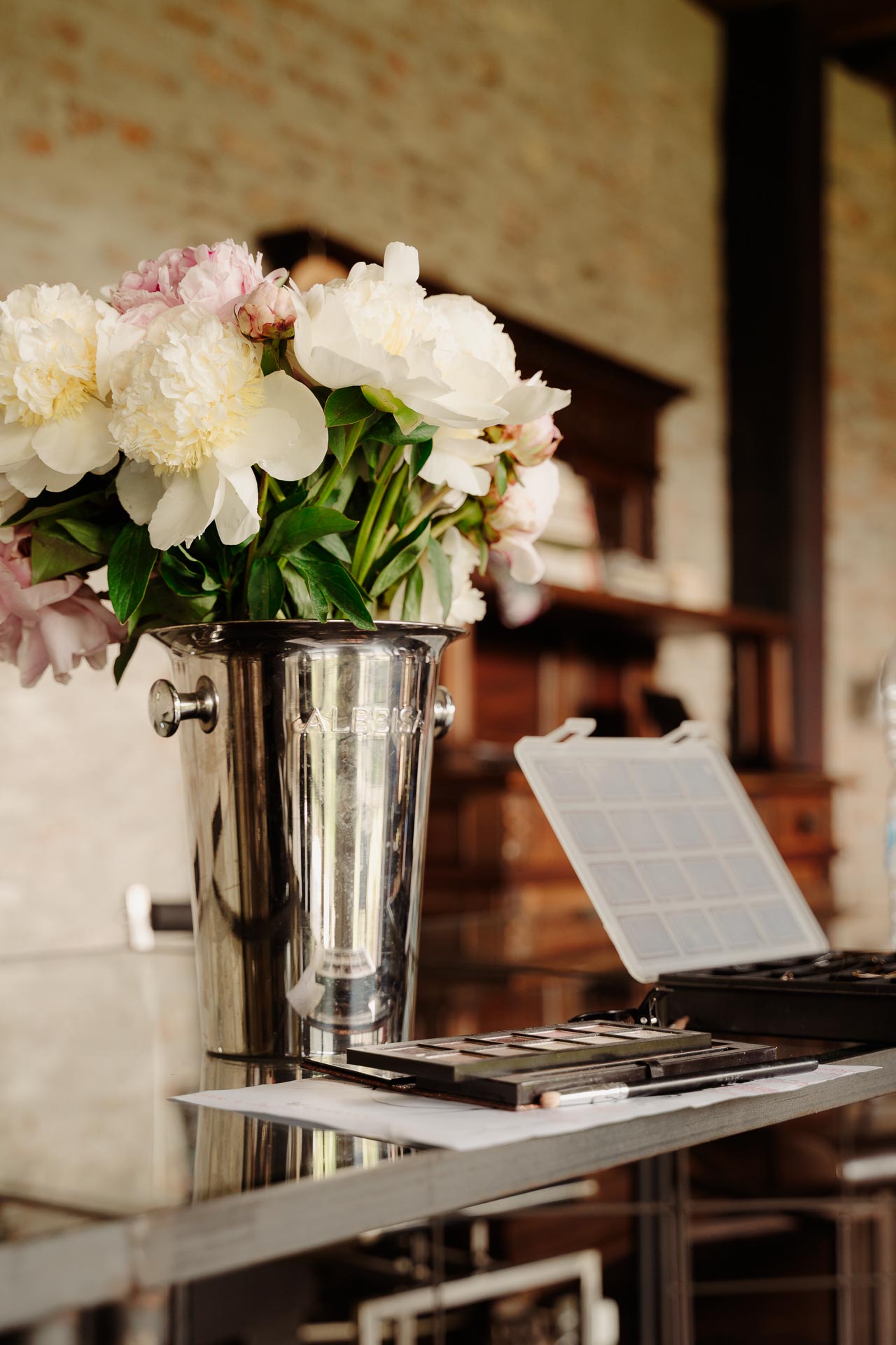 Le peonie in un vaso d'acciaio accanto alla tavolozza dei trucchi