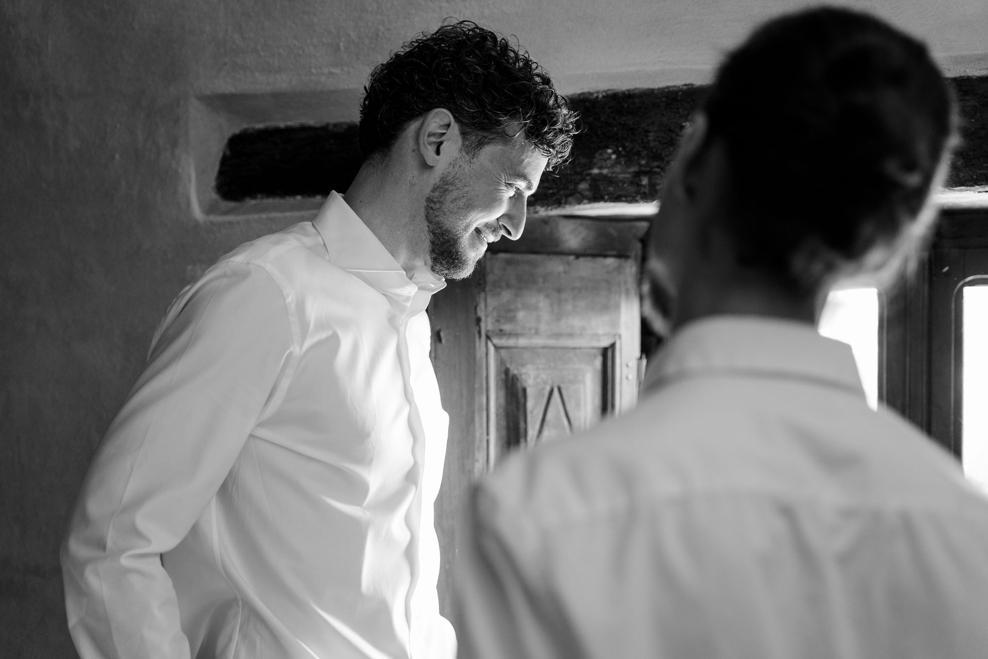 In bianco e nero, lo sposo in camicia bianca sorride a un amico