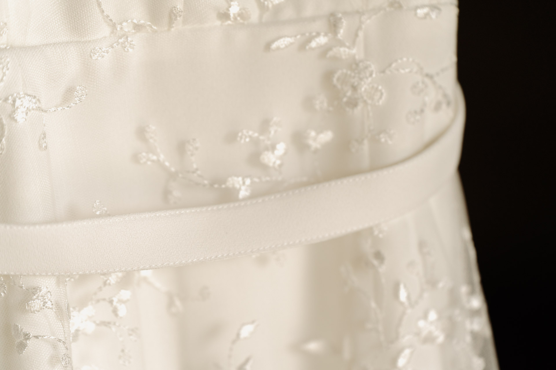 Il pizzo ricamato dell'abito da sposa e la cintura di raso