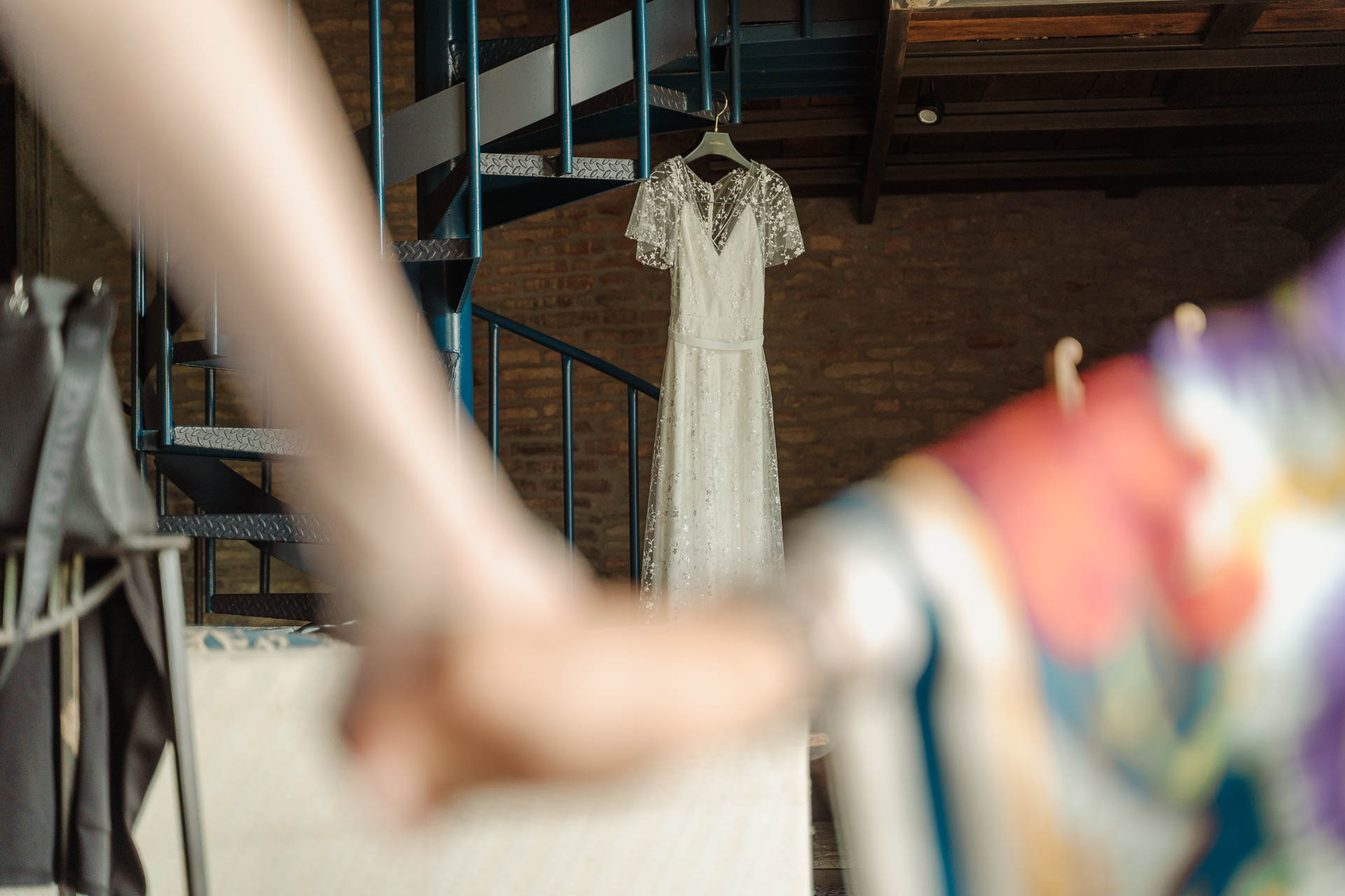 L'abito da sposa appeso alla scala a chiocciola, visto oltre il braccio di un'amica