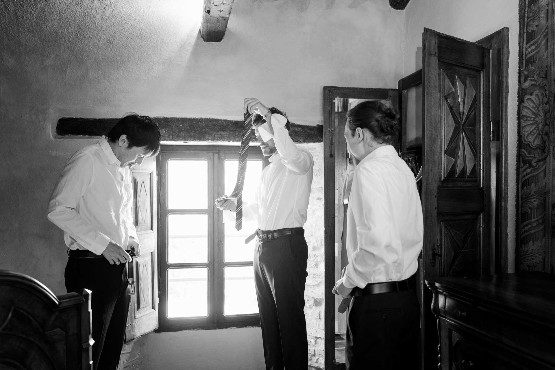 In bianco e nero, lo sposo e due amici in camicia bianca si preparano nella camera