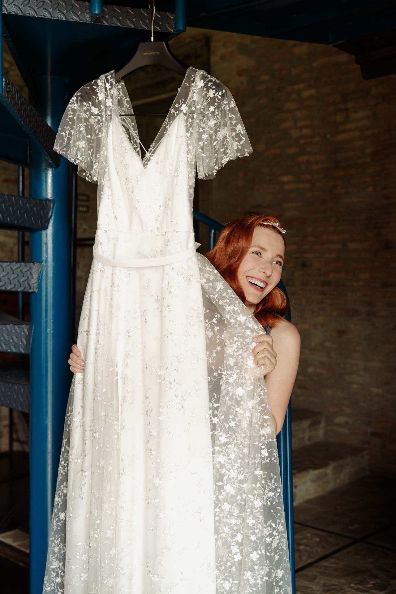La sposa ride, nascosta dietro l'abito appeso alla scala a chiocciola