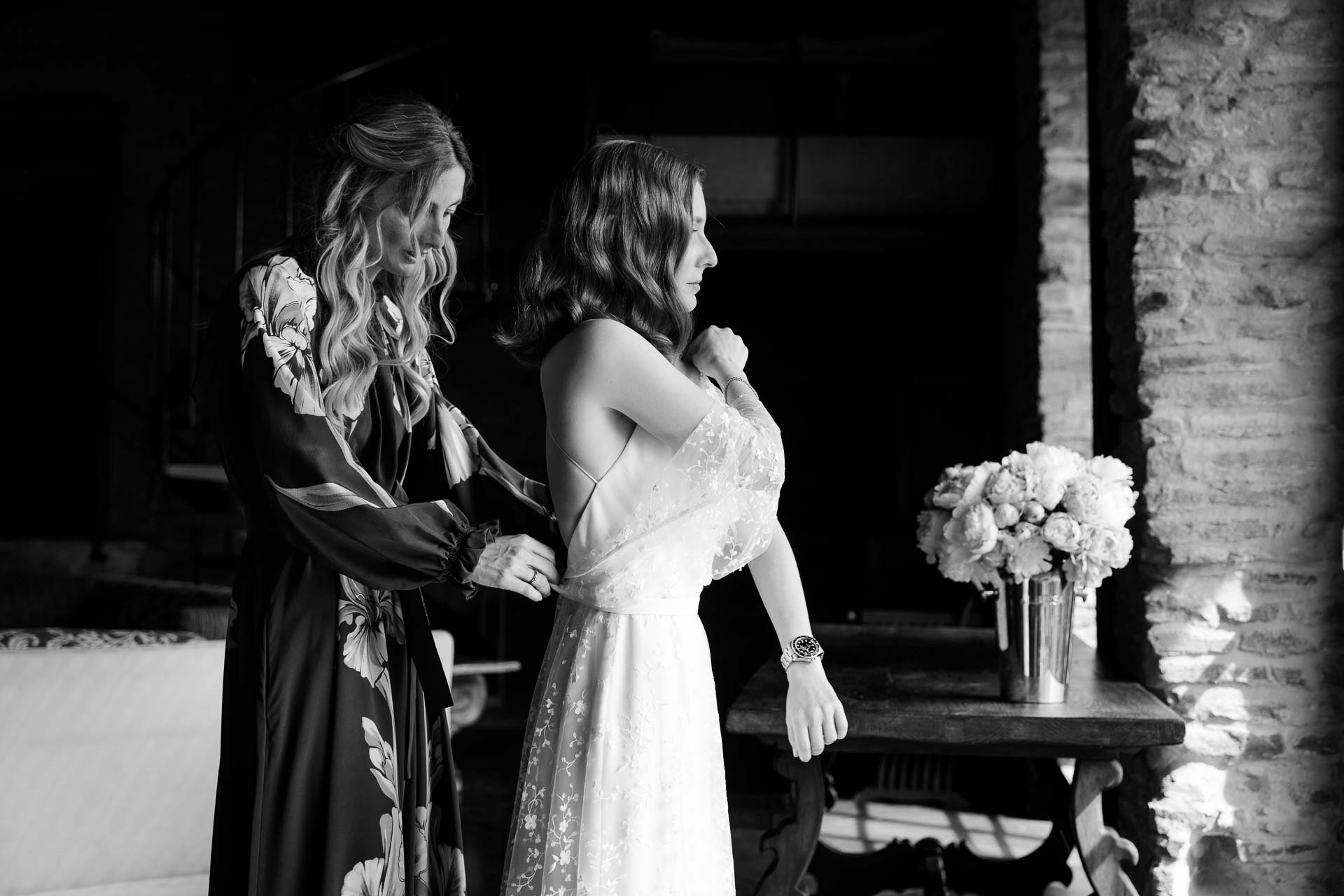 In bianco e nero, un'amica in vestaglia a fiori aiuta la sposa con l'abito