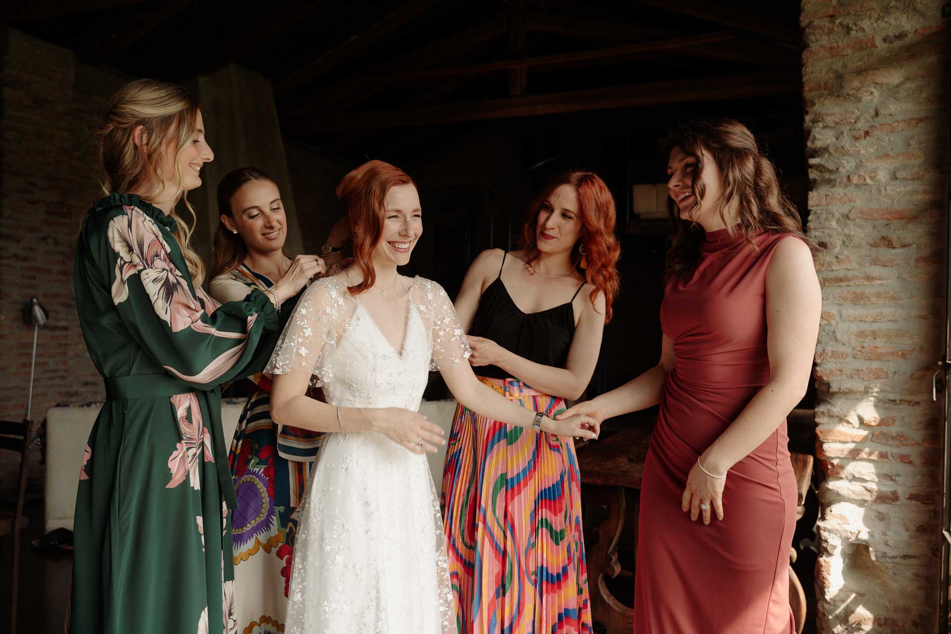 La sposa sorride tra le amiche in abiti colorati, che le sistemano l'abito