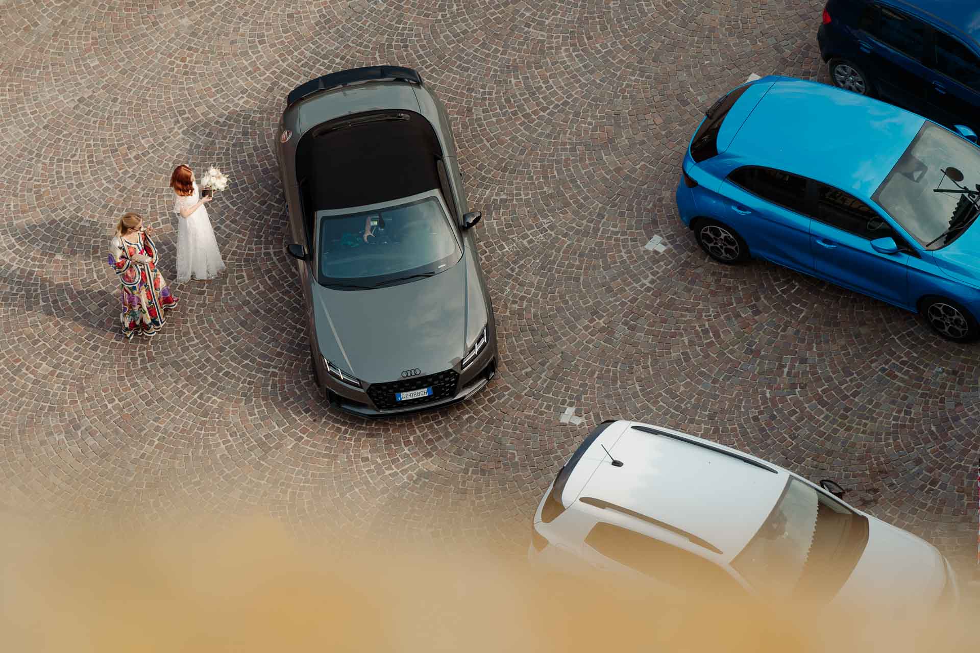 Dall'alto della torre, la sposa e una bambina attraversano la piazza tra le auto