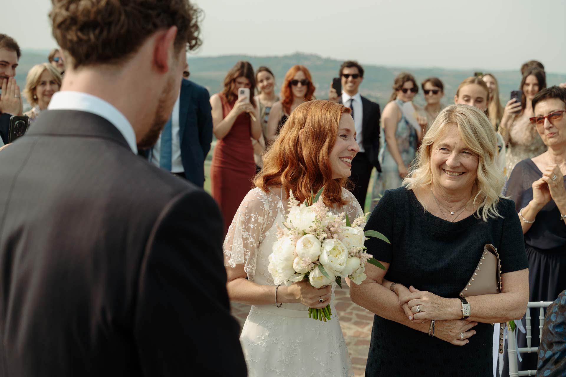 La sposa con il bouquet arriva davanti allo sposo, accanto a una donna sorridente
