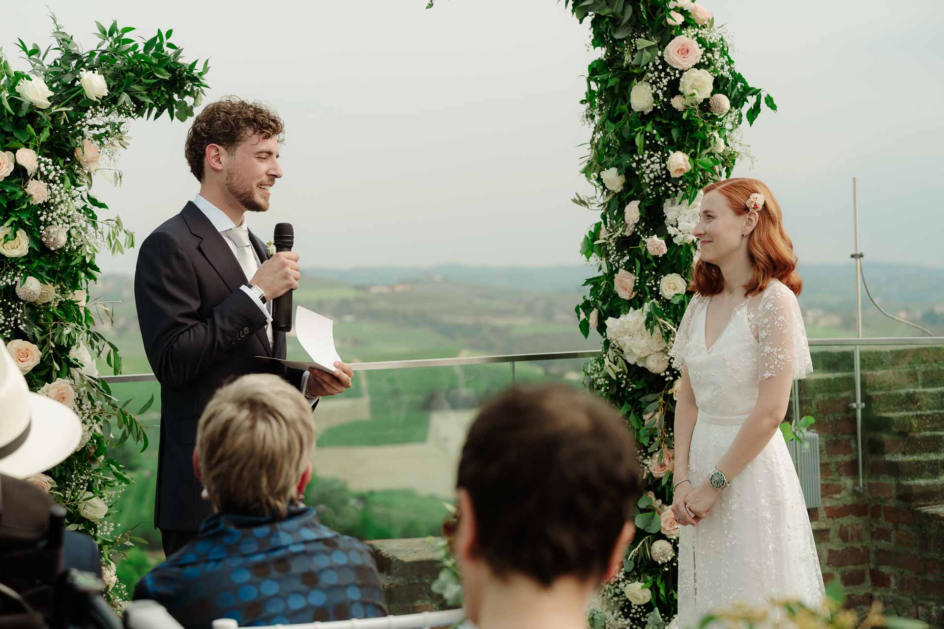 Lo sposo legge le promesse al microfono, davanti alla sposa che sorride