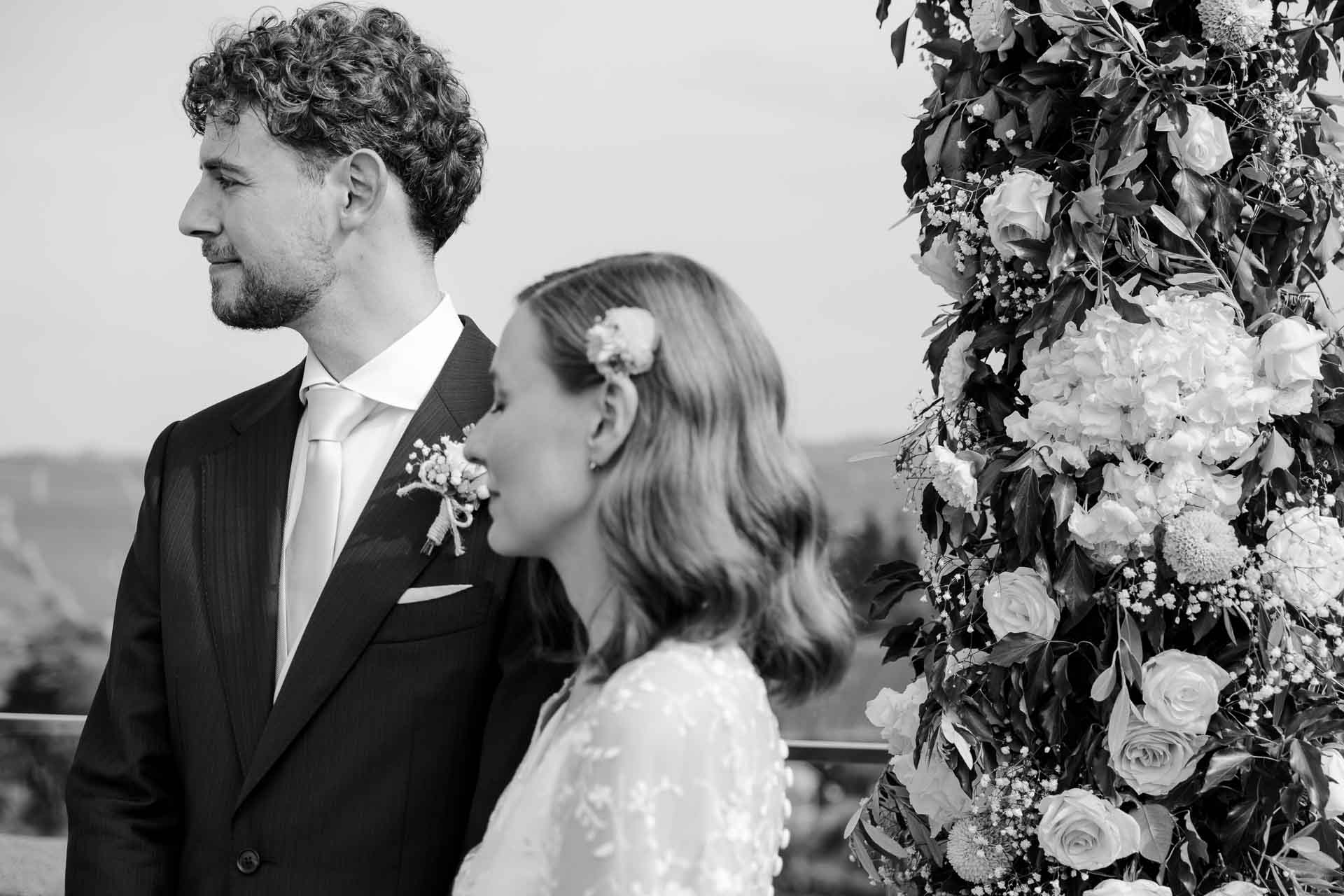 In bianco e nero, lo sposo guarda la sposa accanto alle rose dell'arco