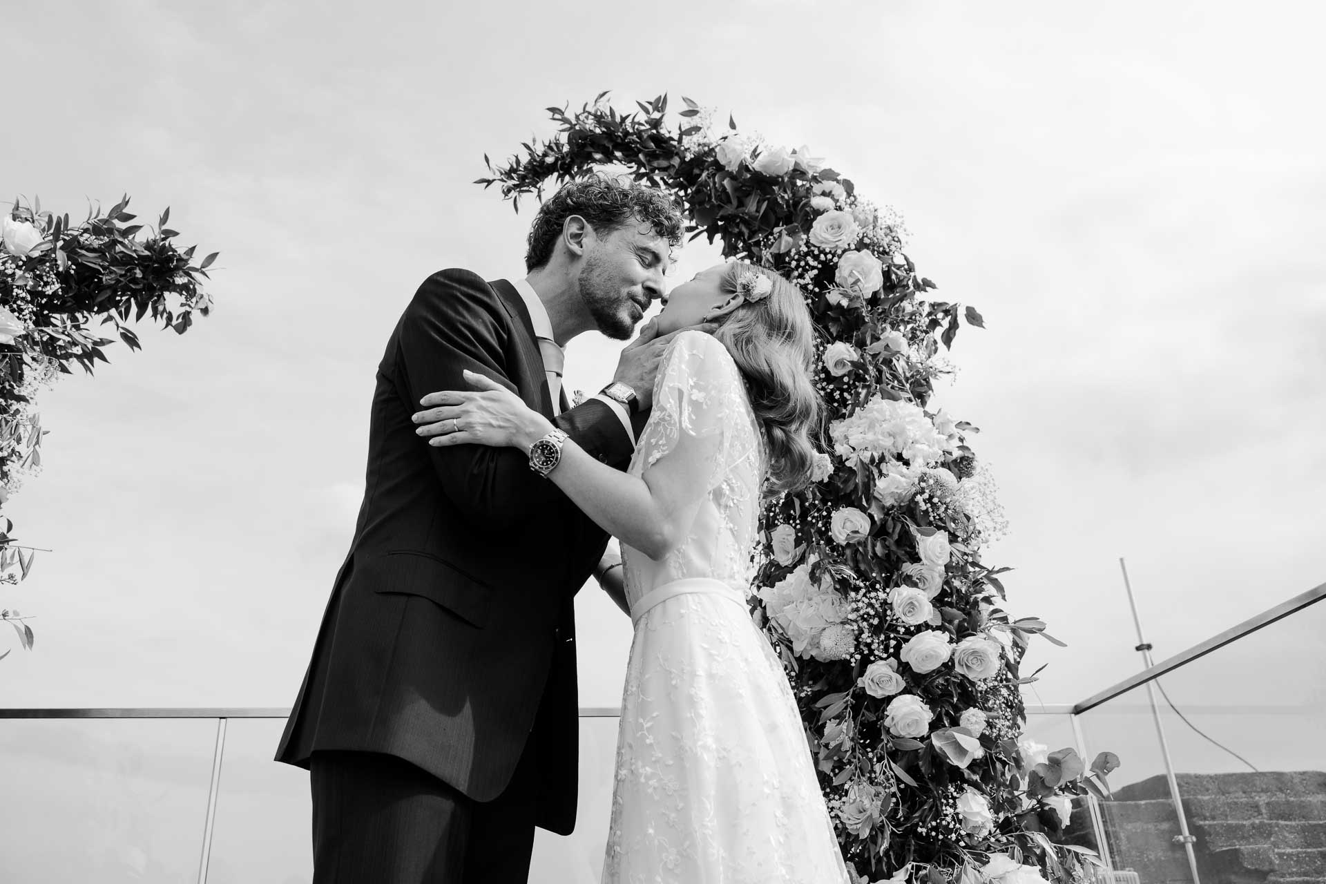 In bianco e nero, il bacio degli sposi sotto l'arco di fiori