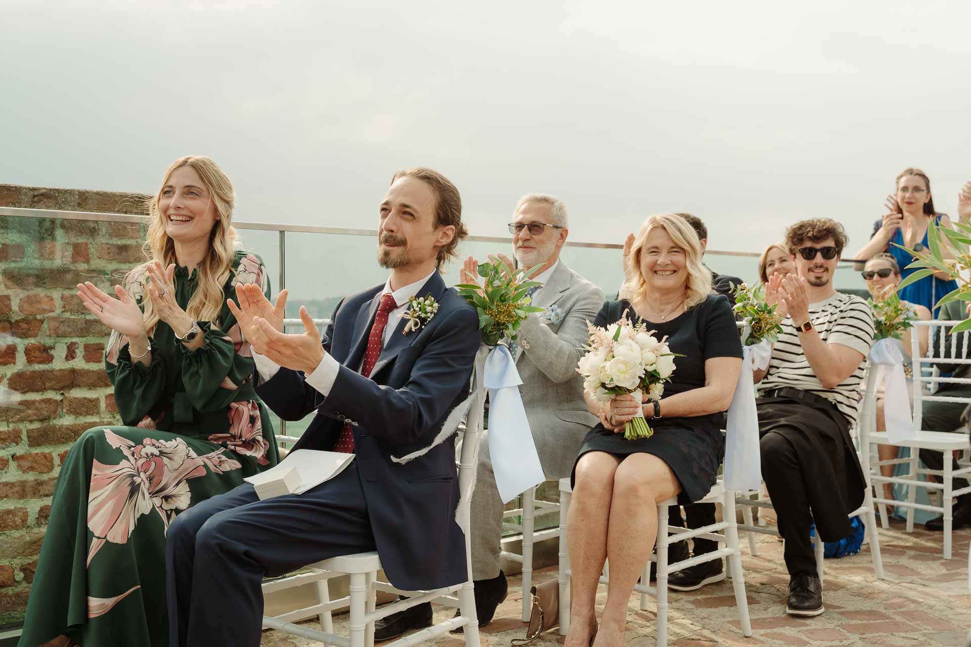 Gli invitati applaudono, seduti sulle sedie bianche